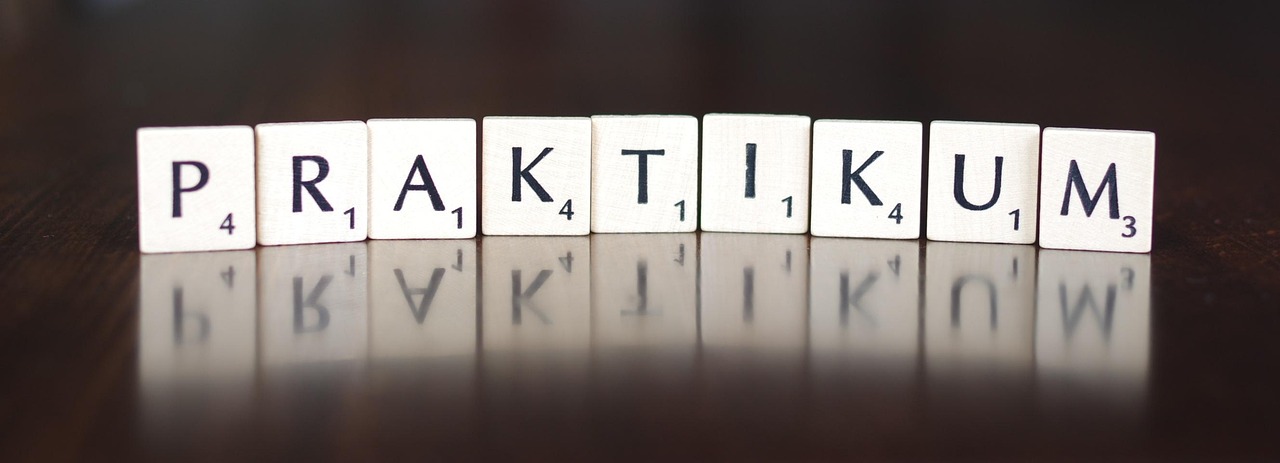 Litery na kafelkach tworzą słowo PRAKTIKUM, nawiązując do tematu staży.