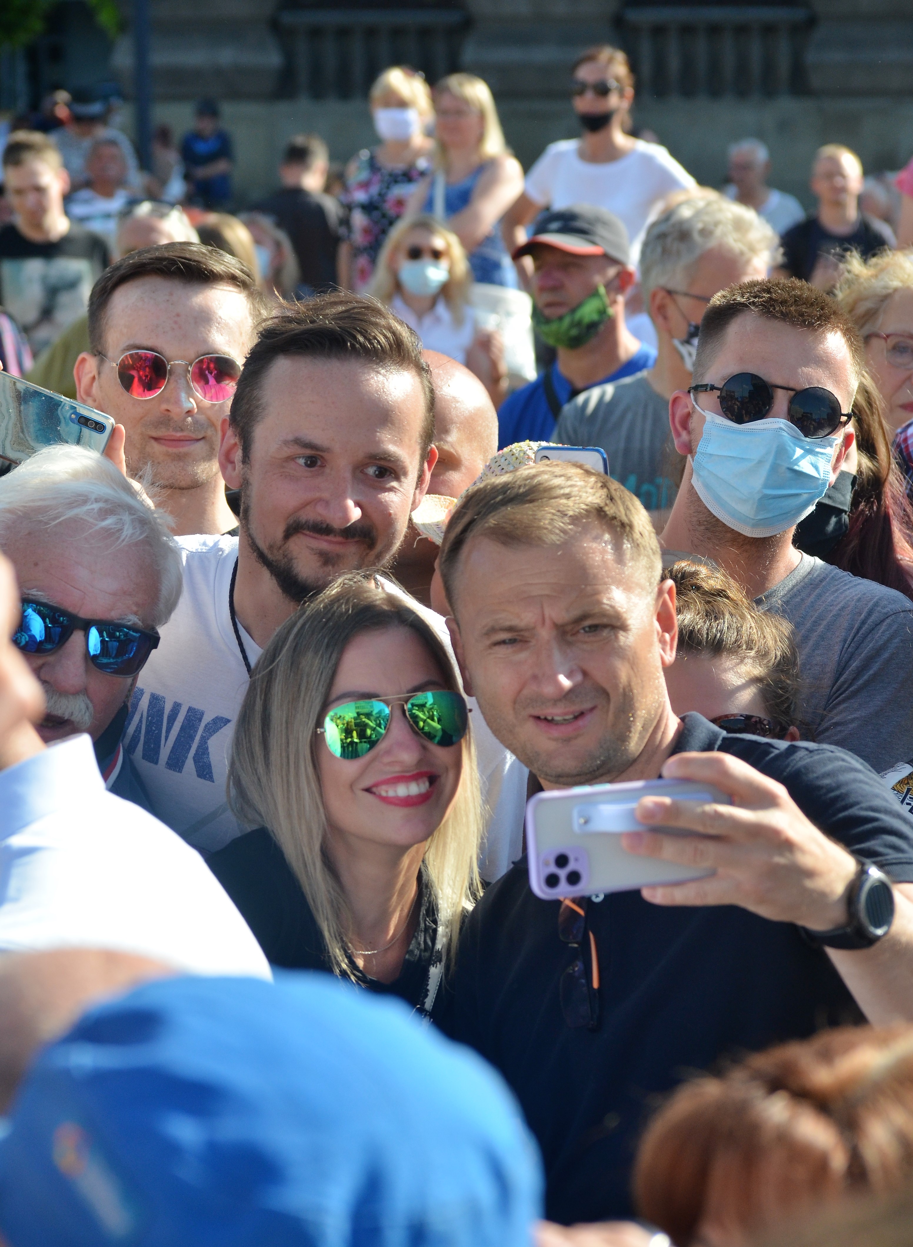 Ludzie robiący selfie na tle tłumu, nawiązujące do zmian w rządzie.