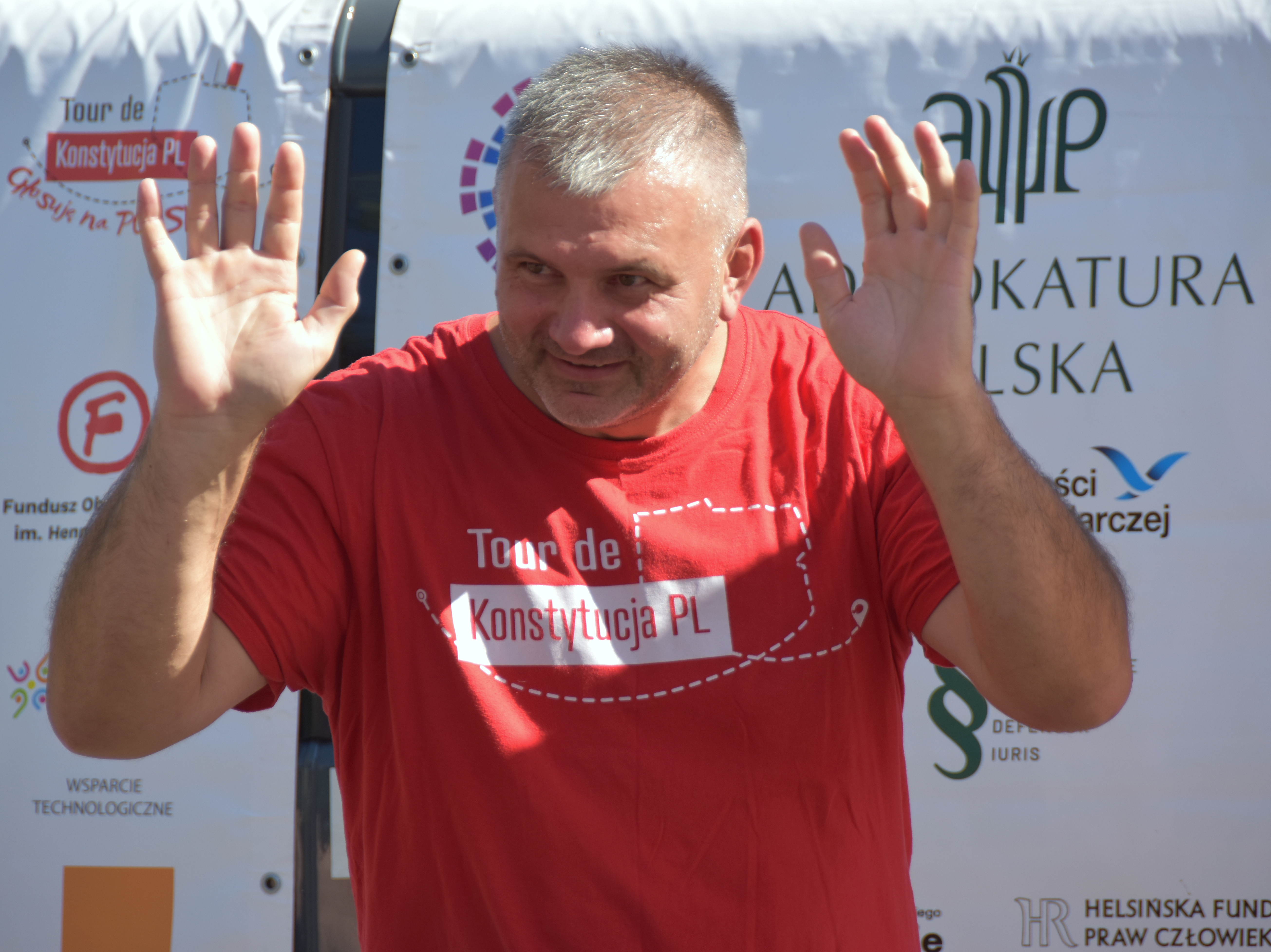 Sędzia Waldemar Żurek w czerwonej koszulce z napisem "Tour de Konstytucja PL" podnosi ręce.