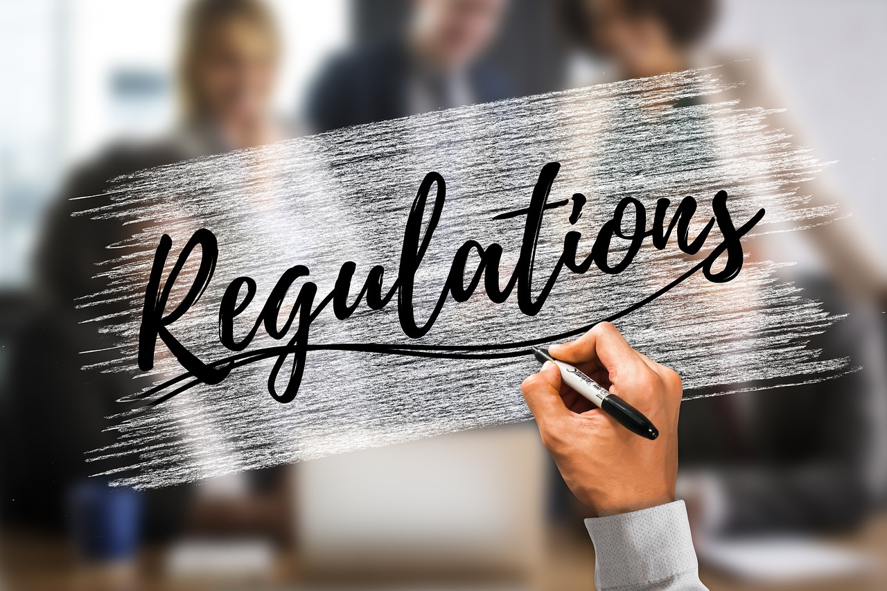 Ręka pisze słowo "Regulations" na tle rozmazanych ludzi, symbolizując polskie przepisy.