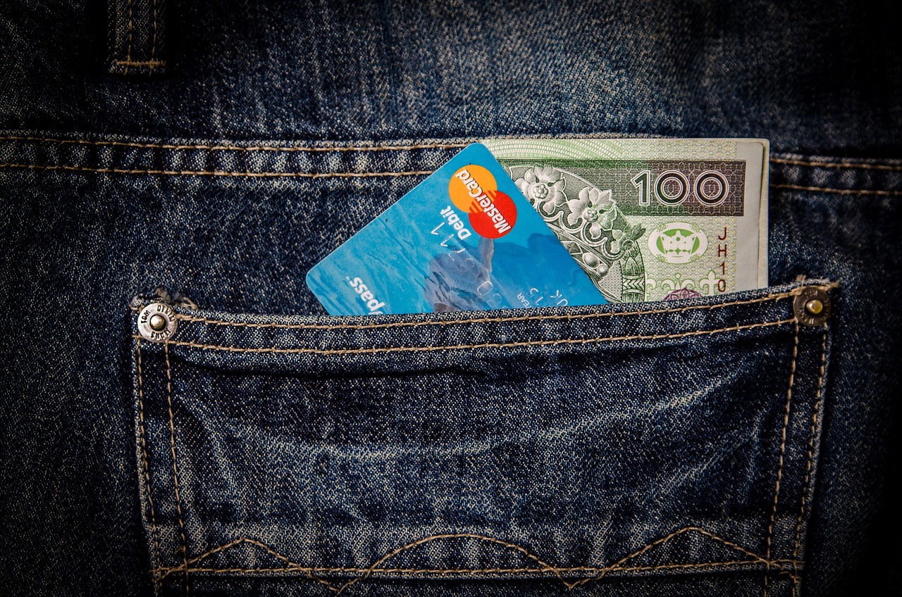 Karta płatnicza i banknot w kieszeni dżinsów – symbol oszczędnych wyjazdów jesienią.