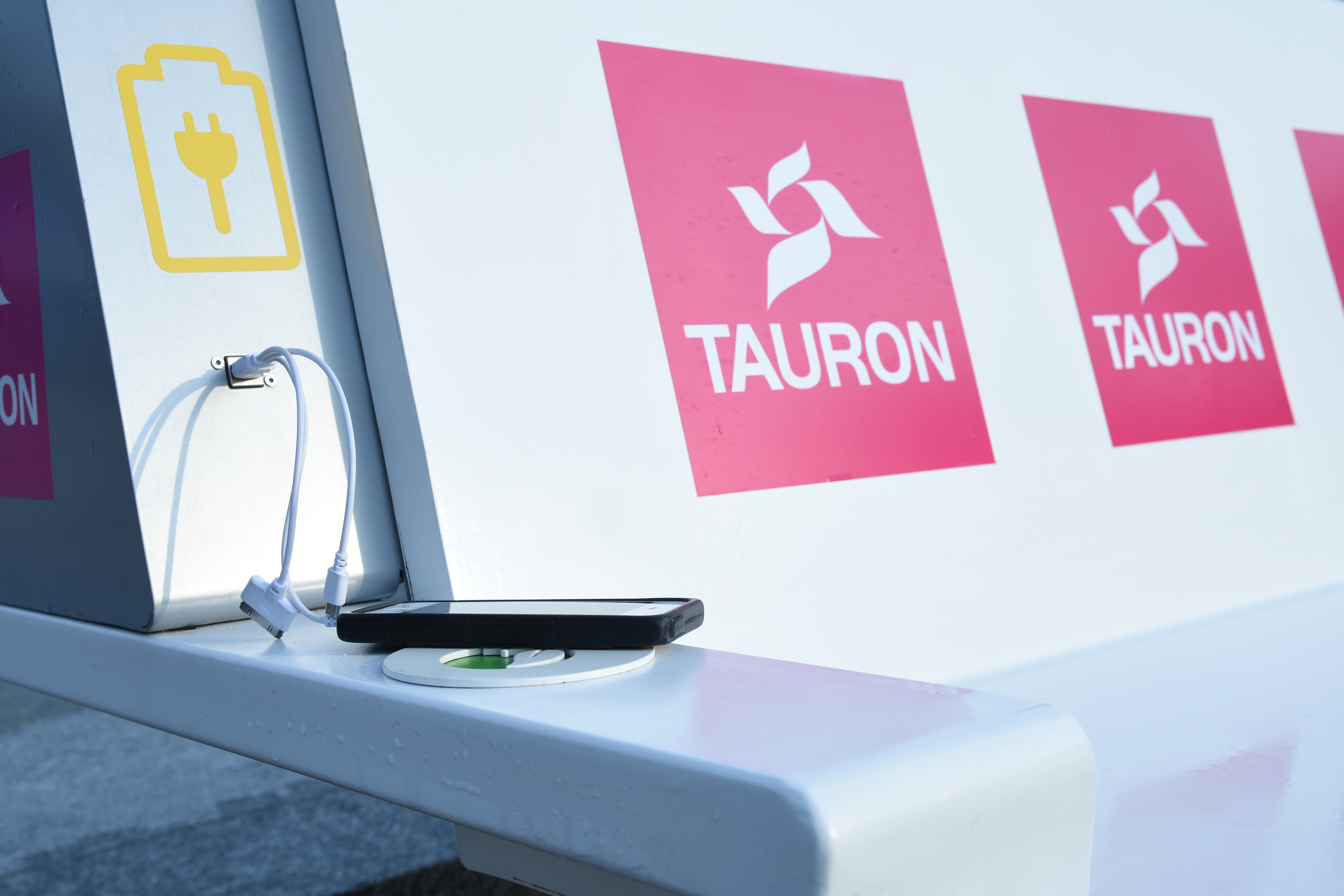 Stacja ładowania Tauron z telefonem i kablami, symbolizująca rozwój energetyczny.