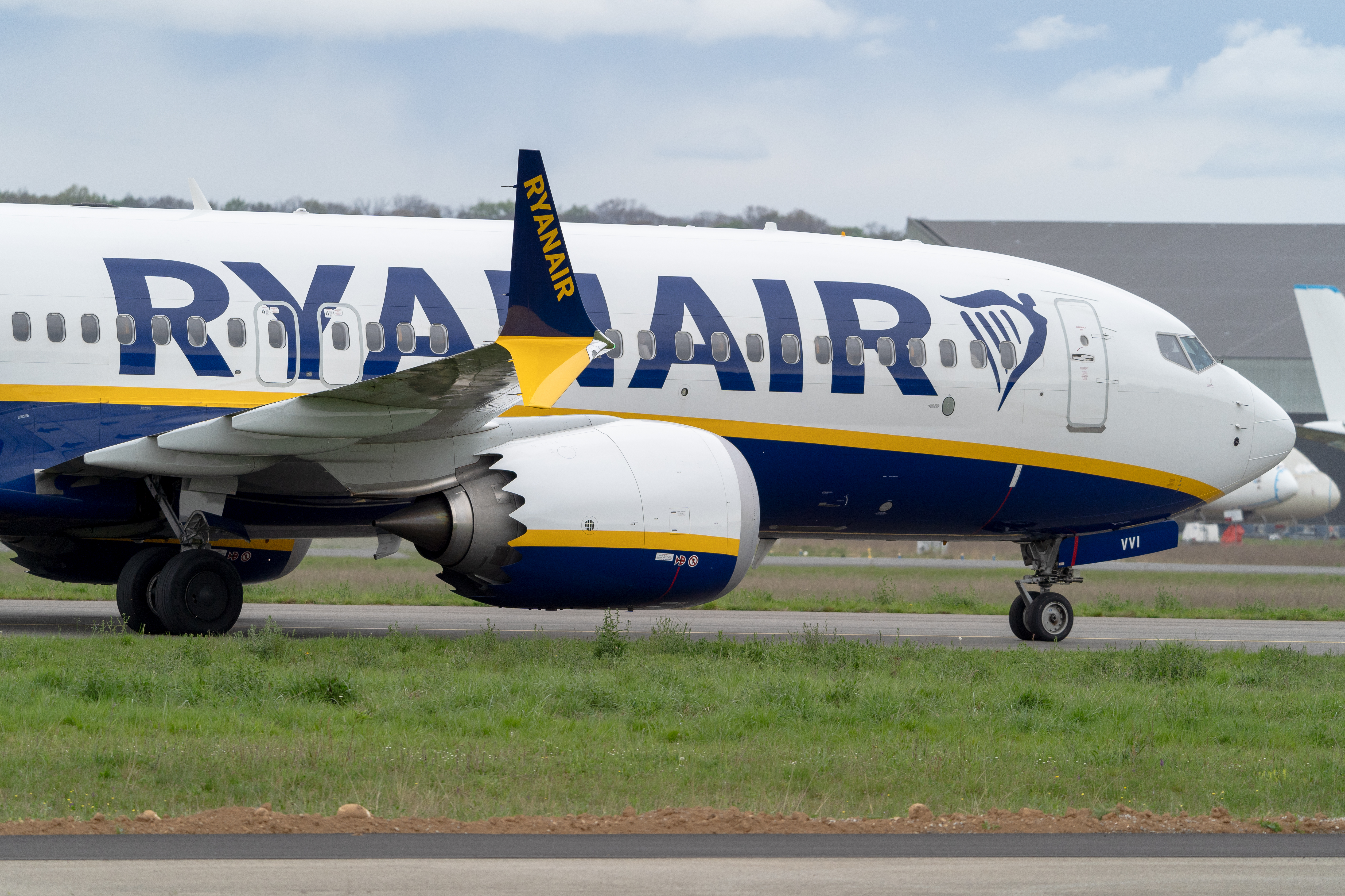 Samolot linii Ryanair na płycie lotniska, z widocznym logo i silnikiem.