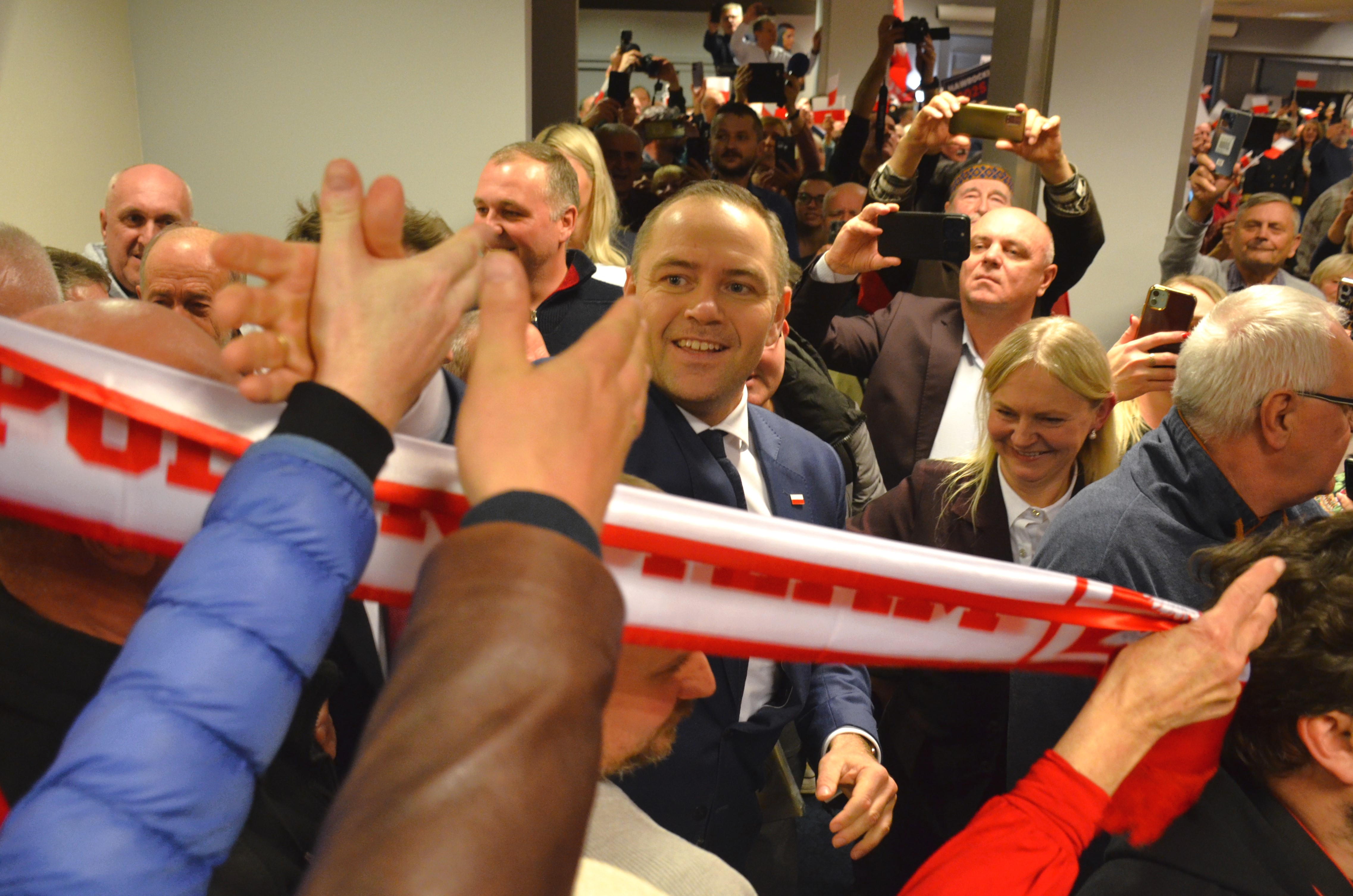 Prezydent Karol Nawrocki w tłumie podczas wydarzenia politycznego, z flagą Polski.