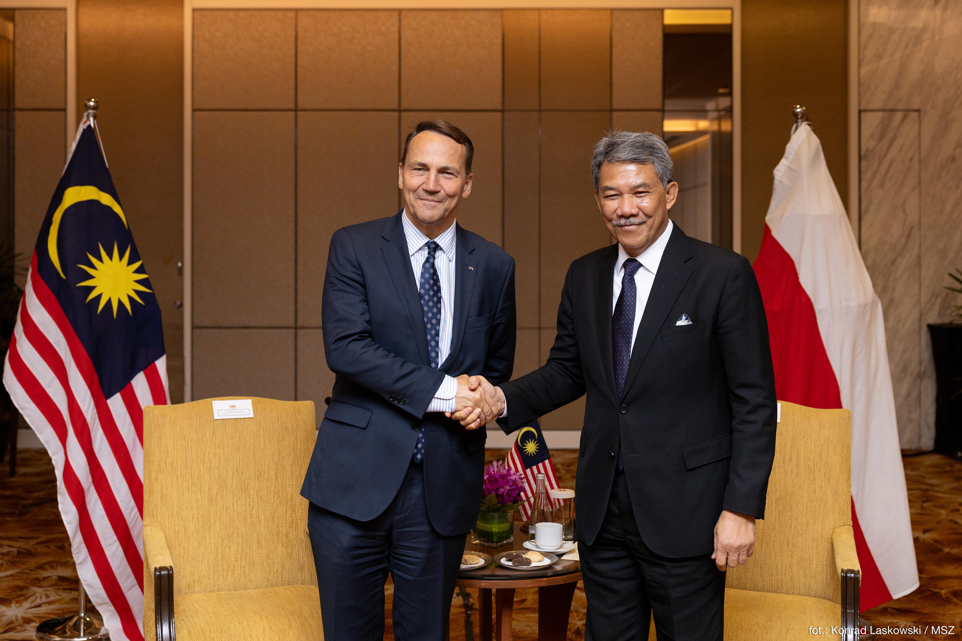 Radosław Sikorski i Dato' Seri Mohamed Azmin Ali uściski dłoni z flagami Malezji i Polski.
