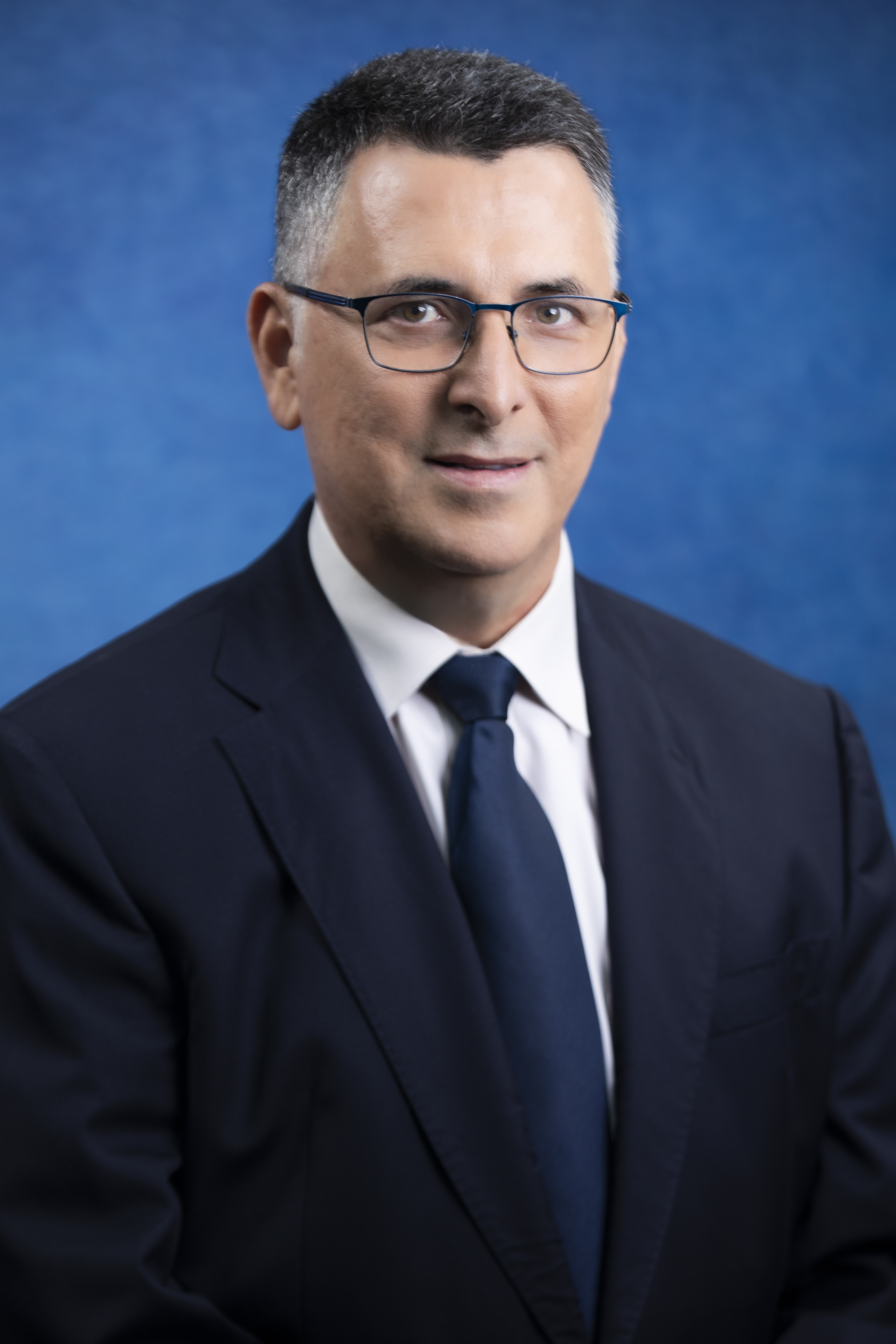Szef izraelskiego MSZ Gideon Saar w garniturze i krawacie, na tle niebieskim.