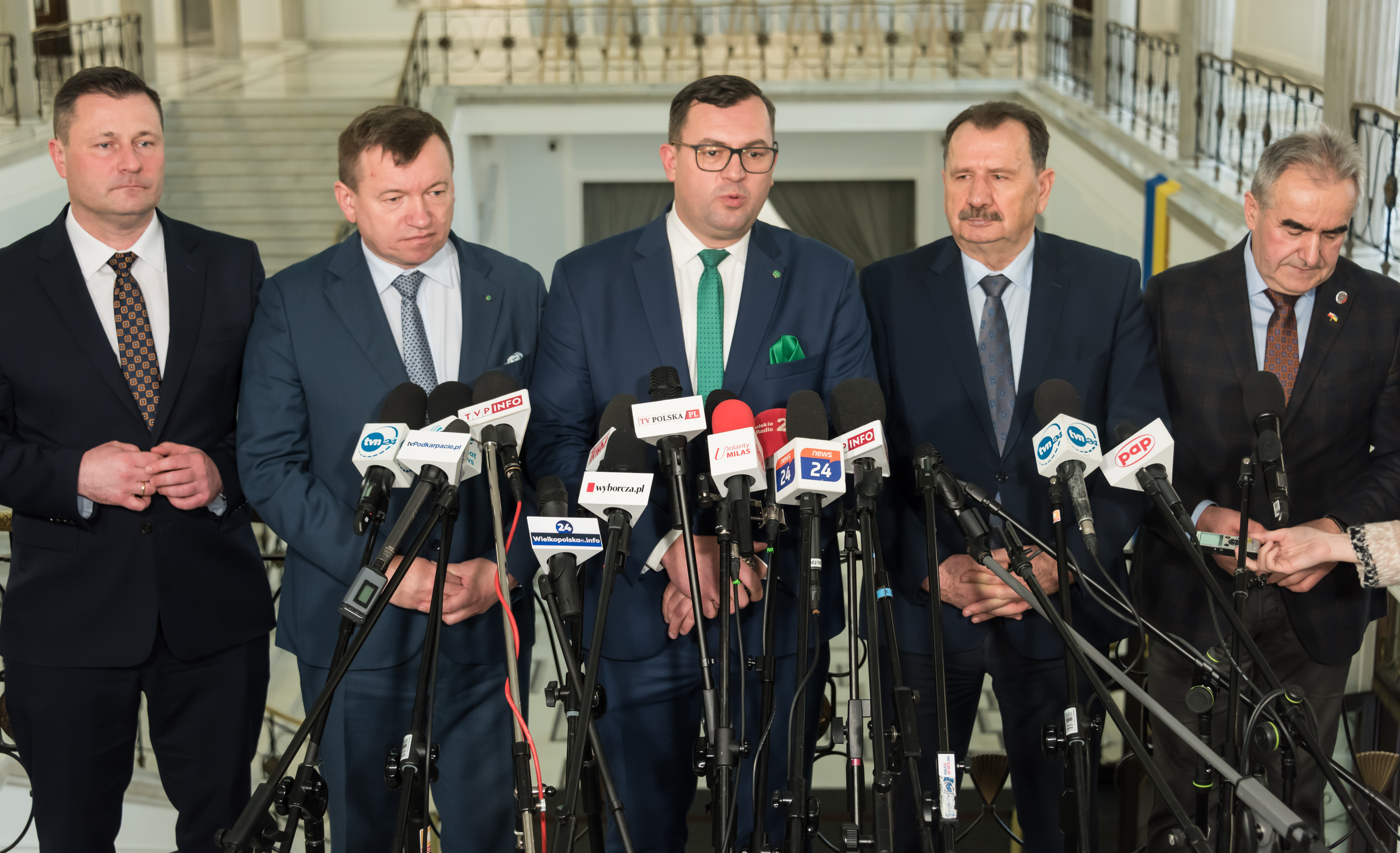 Stefan Krajewski podczas wywiadu z mediami, otoczony przez dziennikarzy i mikrofony.