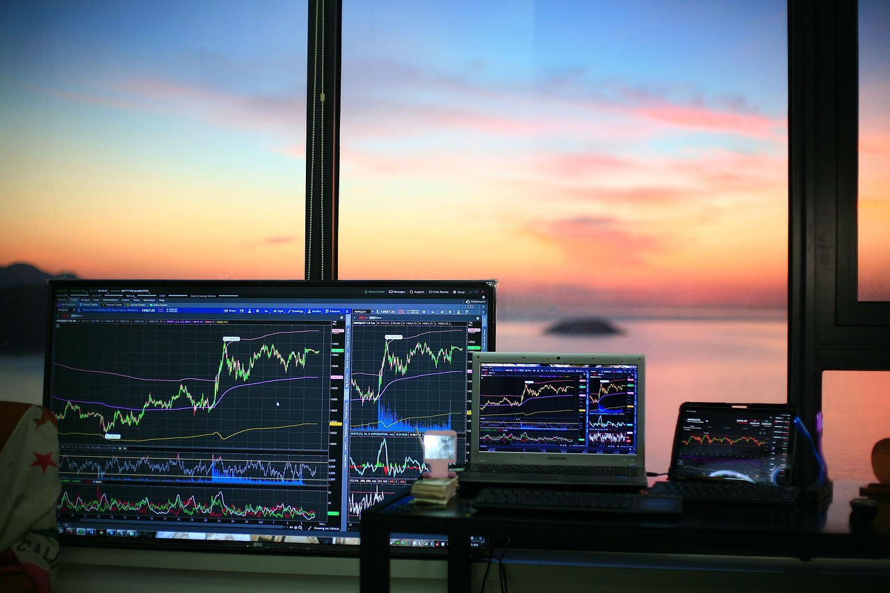 Wielokrotne monitory z wykresami giełdowymi S&P 500 na tle zachodu słońca, symbolizujące analizę rynkową.