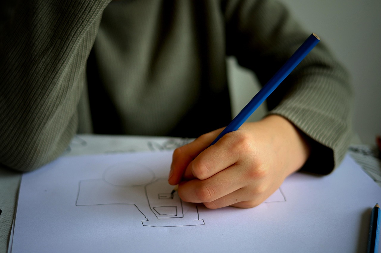 Dłoń dziecka rysująca ołówkiem na kartce papieru, symbolizująca proces nauczania i edukacji.