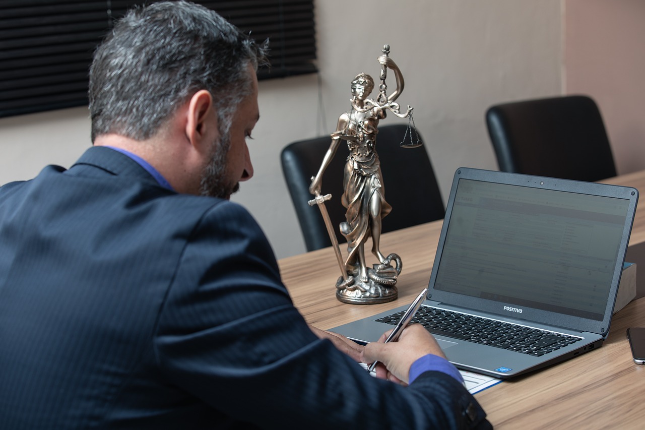 Prawnik analizuje dokumenty na laptopie, obok stoi Statua Sprawiedliwości.