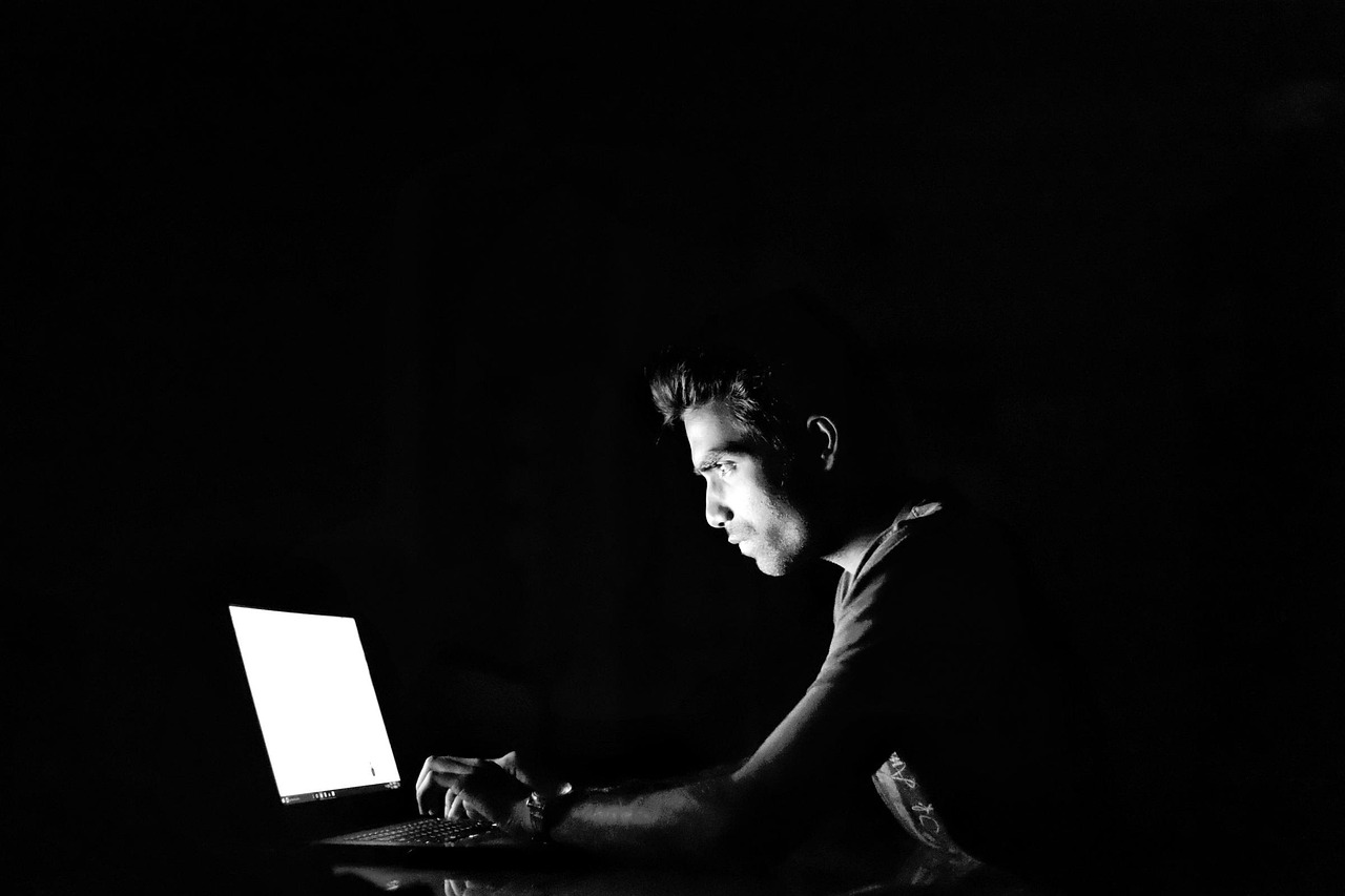 Mężczyzna pracujący na laptopie w ciemności, symbolizujący cyberatak w motoryzacji.