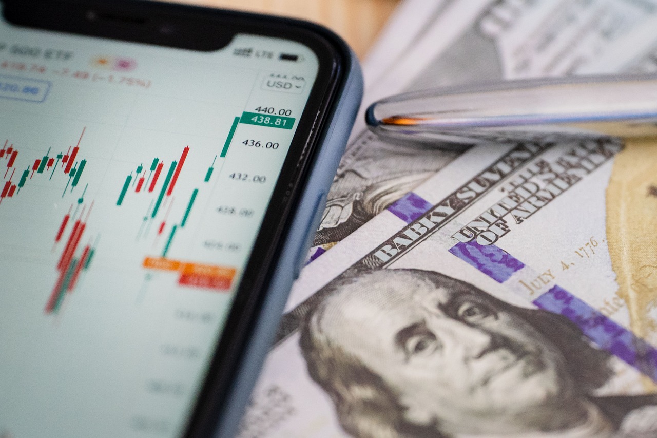Wykres giełdowy na smartfonie i banknoty dolarowe, ilustrujące straty na giełdzie.