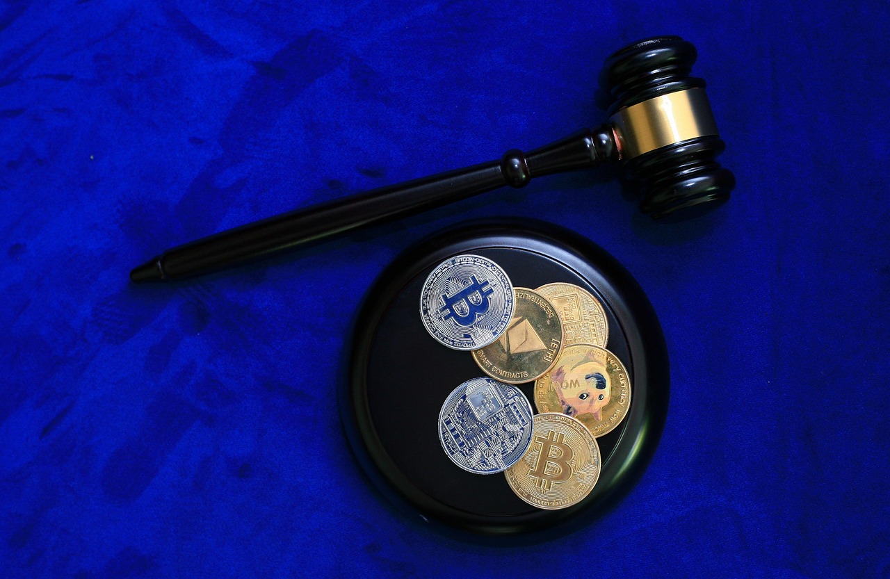Młotek sędziowski i monety kryptowalutowe, w tym Bitcoin i Ethereum, na niebieskim tle.