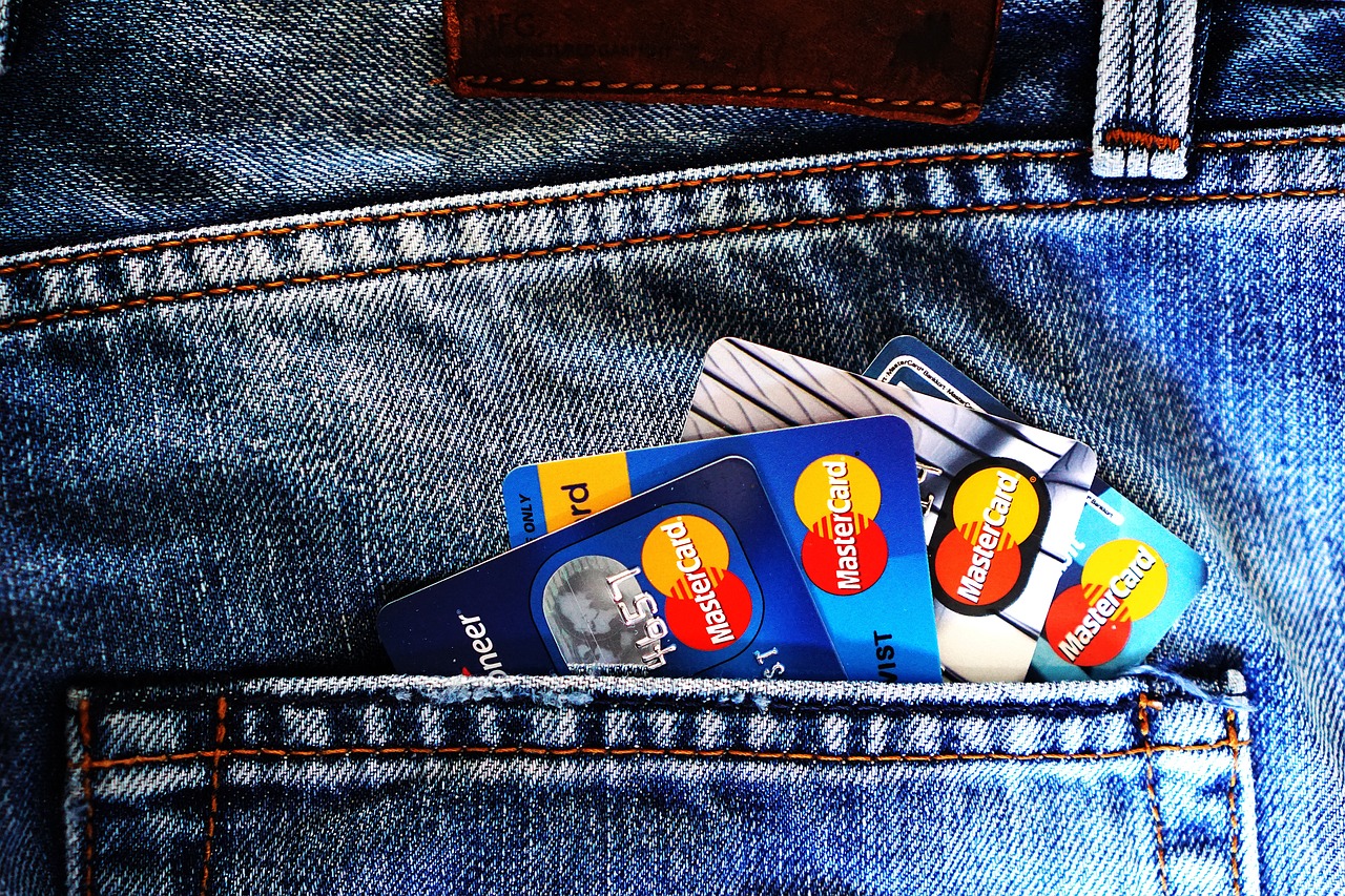 Karta płatnicza MasterCard w kieszeni jeansów, symbol fuzji bankowej.