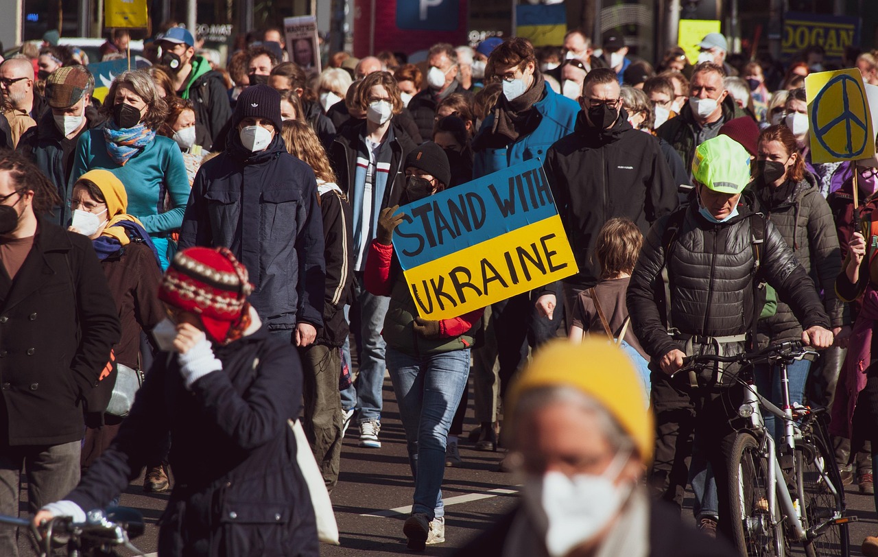 Protestujący z transparentem "Stand with Ukraine" w kontekście ostrzeżenia o rozszerzeniu konfliktu.