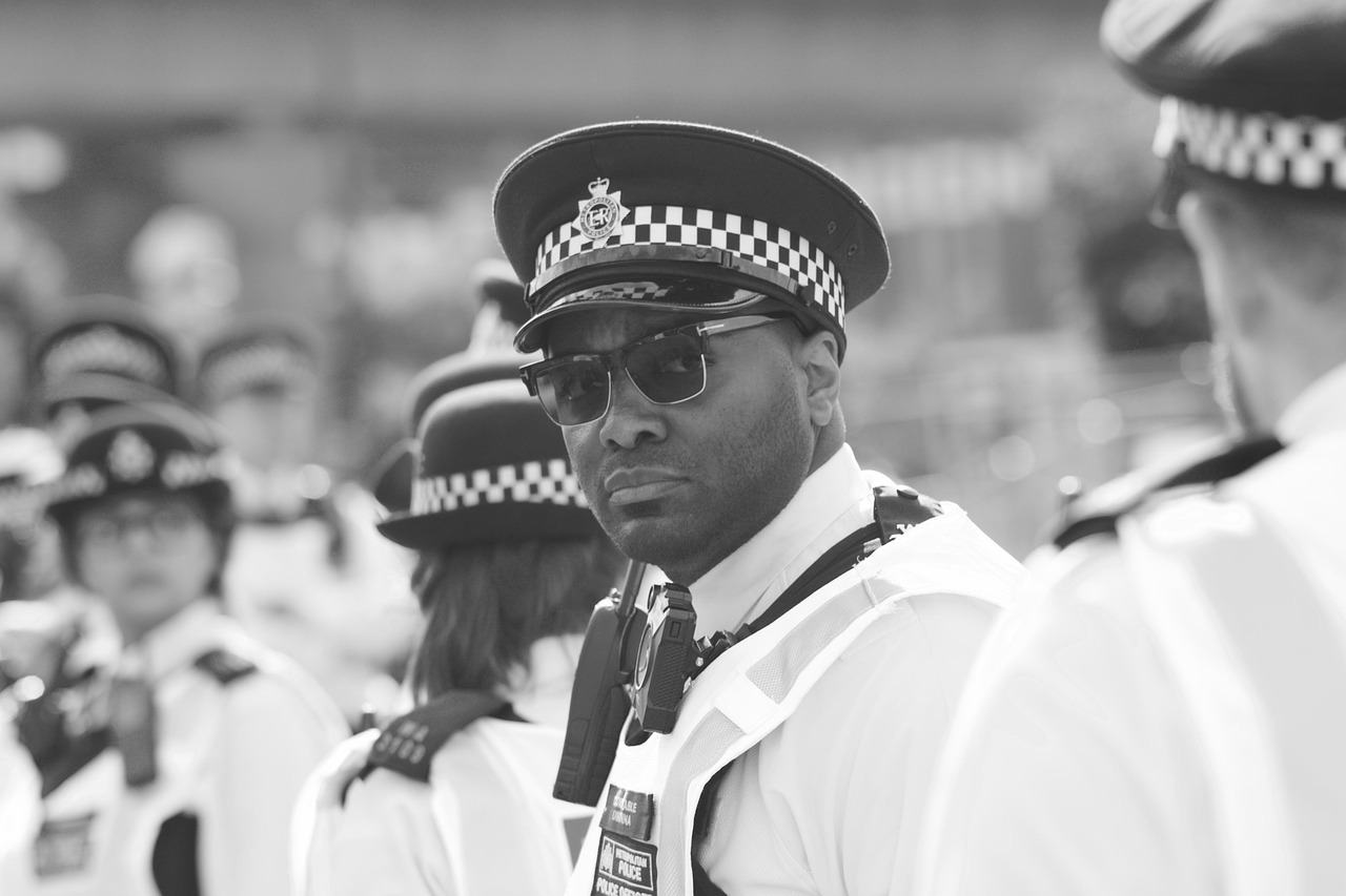 Policjant w okularach przeciwsłonecznych i czapce, symbolizujący interwencję służb w sprawie przemocy i narkotyków.