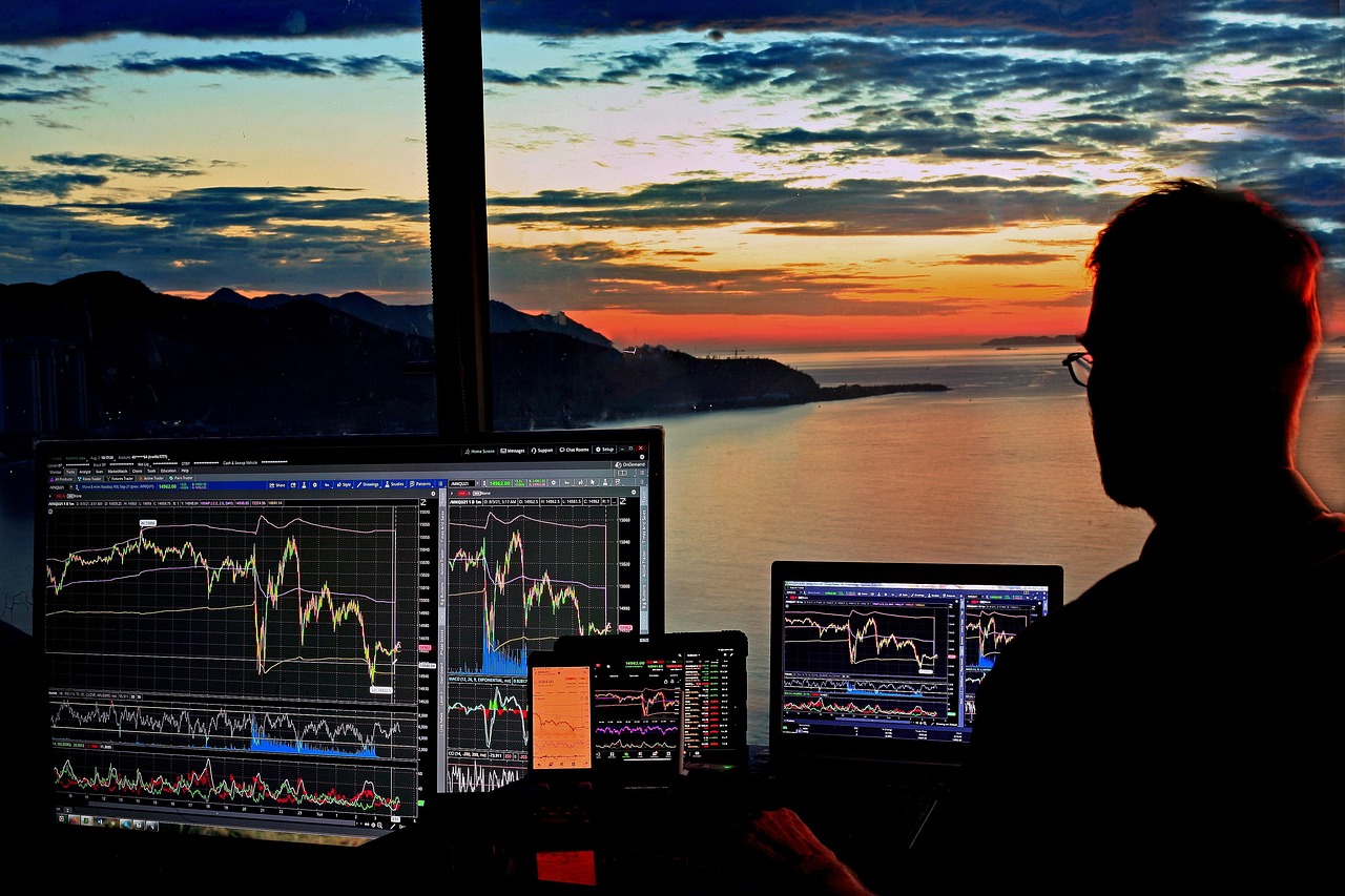 Trader analizujący wykresy giełdowe na wielu monitorach podczas zachodu słońca, ilustrujące przecenę gigantów technologicznych.