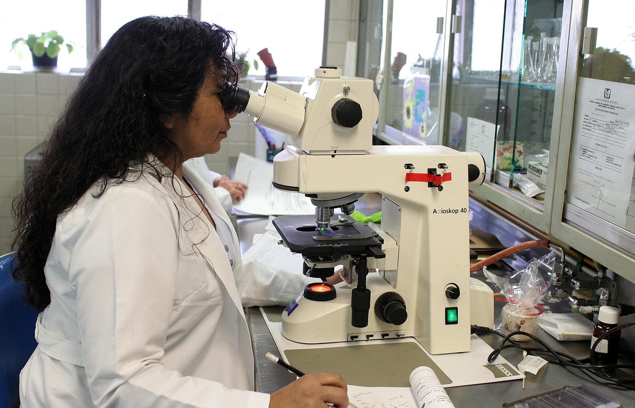 Naukowczyni w białym fartuchu bada próbkę pod mikroskopem w laboratorium, symbolizując badania nad szczepieniami.