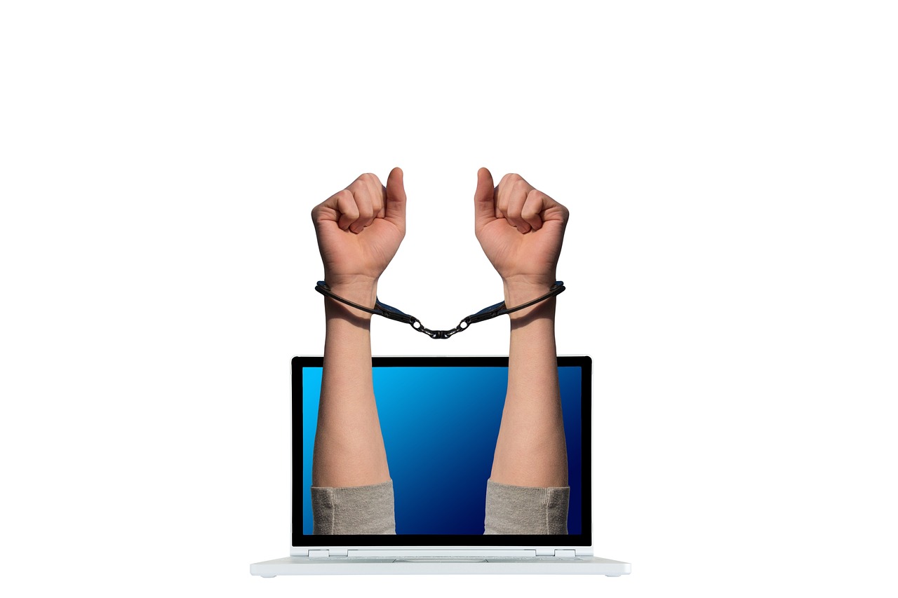 Ręce w kajdankach wychodzące z laptopa, symbolizujące aresztowanie w sprawie siatki terrorystycznej.