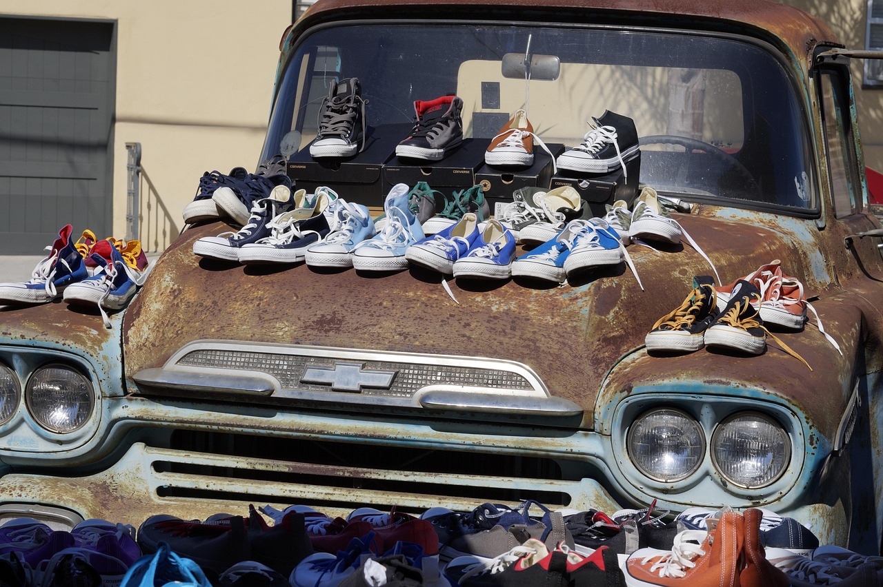 Szeroki wybór sneakersów z drugiej ręki ułożonych na masce starej, zardzewiałej ciężarówki.