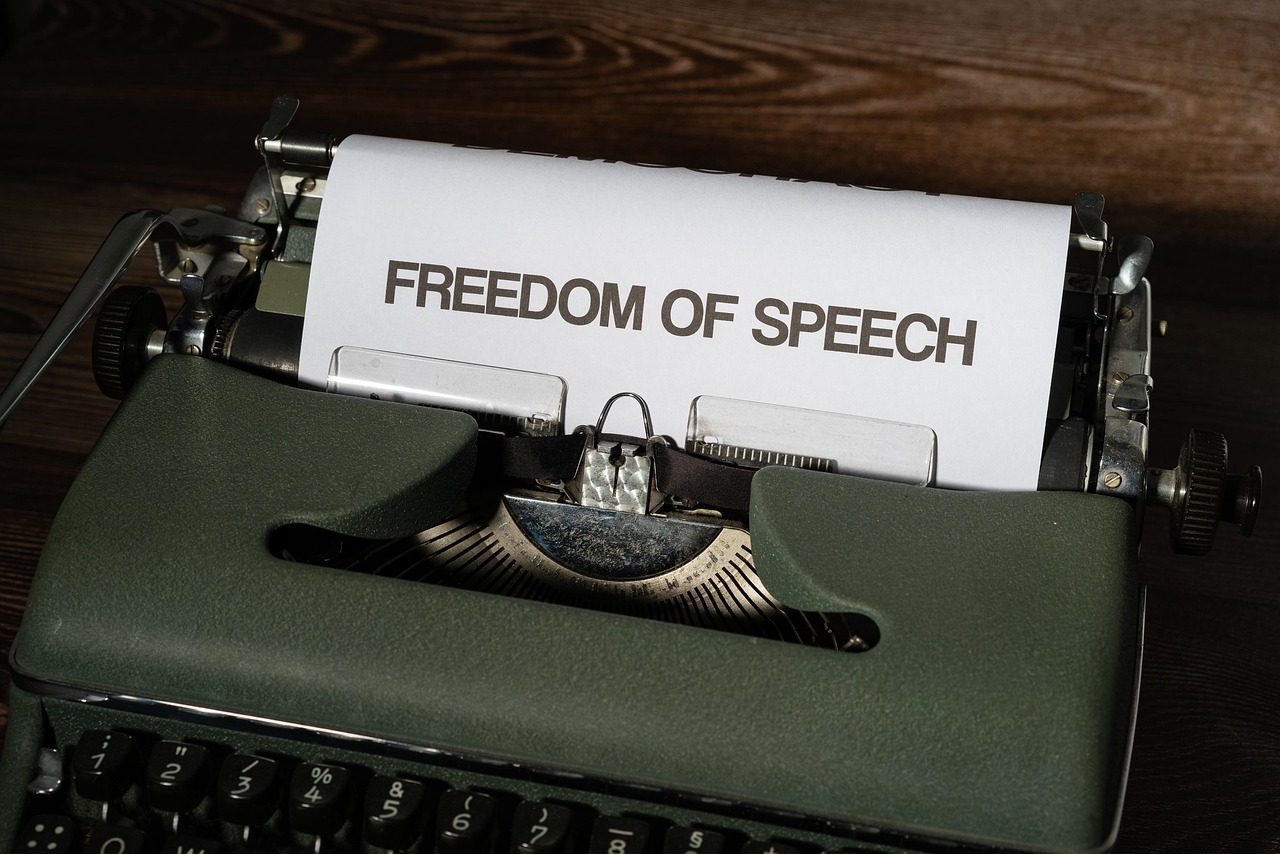 Maszyna do pisania z napisem "FREEDOM OF SPEECH" na papierze, symbolizująca debatę o wolności słowa.