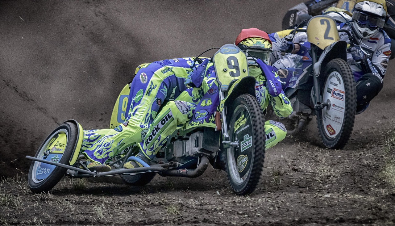 Żużel: zawodnik w żółto-niebieskim kevlarze z numerem 9 na motocyklu ściga się na torze.