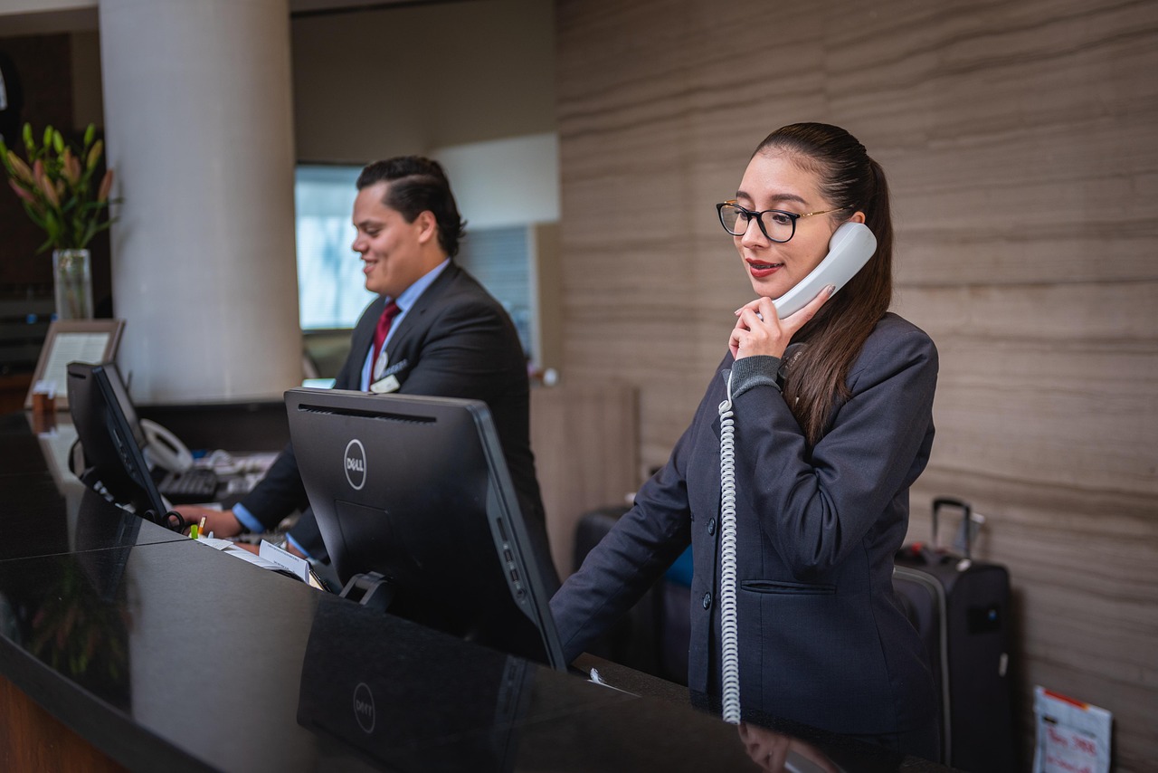 Obsługa klienta w hotelu: Recepcjonistka rozmawia przez telefon, analizując dane klienta.