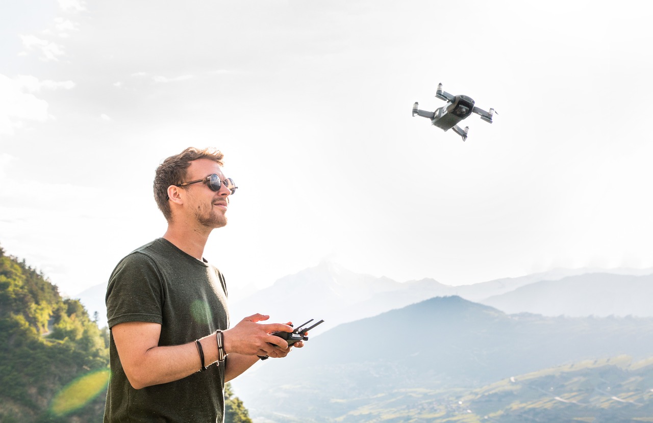 Mężczyzna steruje dronem na tle górskiego krajobrazu, ilustracja zagrożeń w lotnictwie.