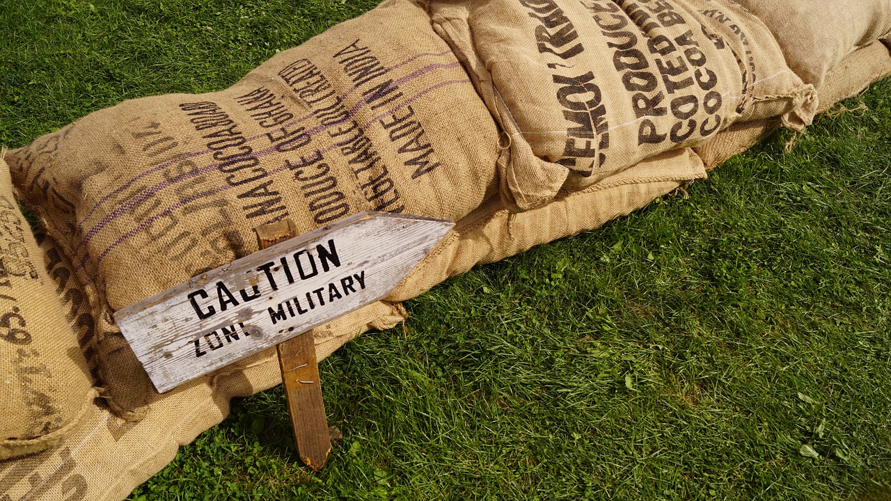 Znak "CAUTION MILITARY ZONE" na tle worków z napisem "PRODUCE OF GHANA" i "MADE IN INDIA".