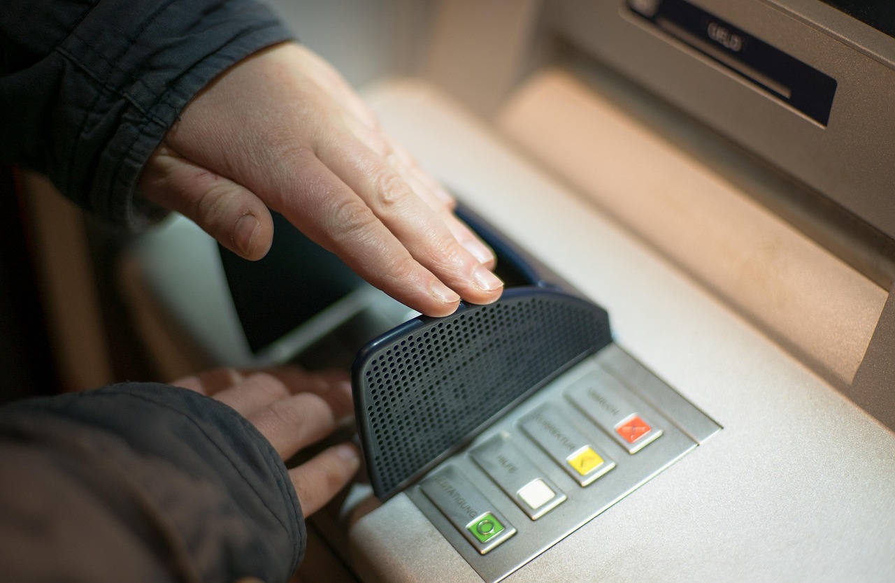 Osoba korzystająca z bankomatu, potencjalne ryzyko scamu i ochrony kapitału.