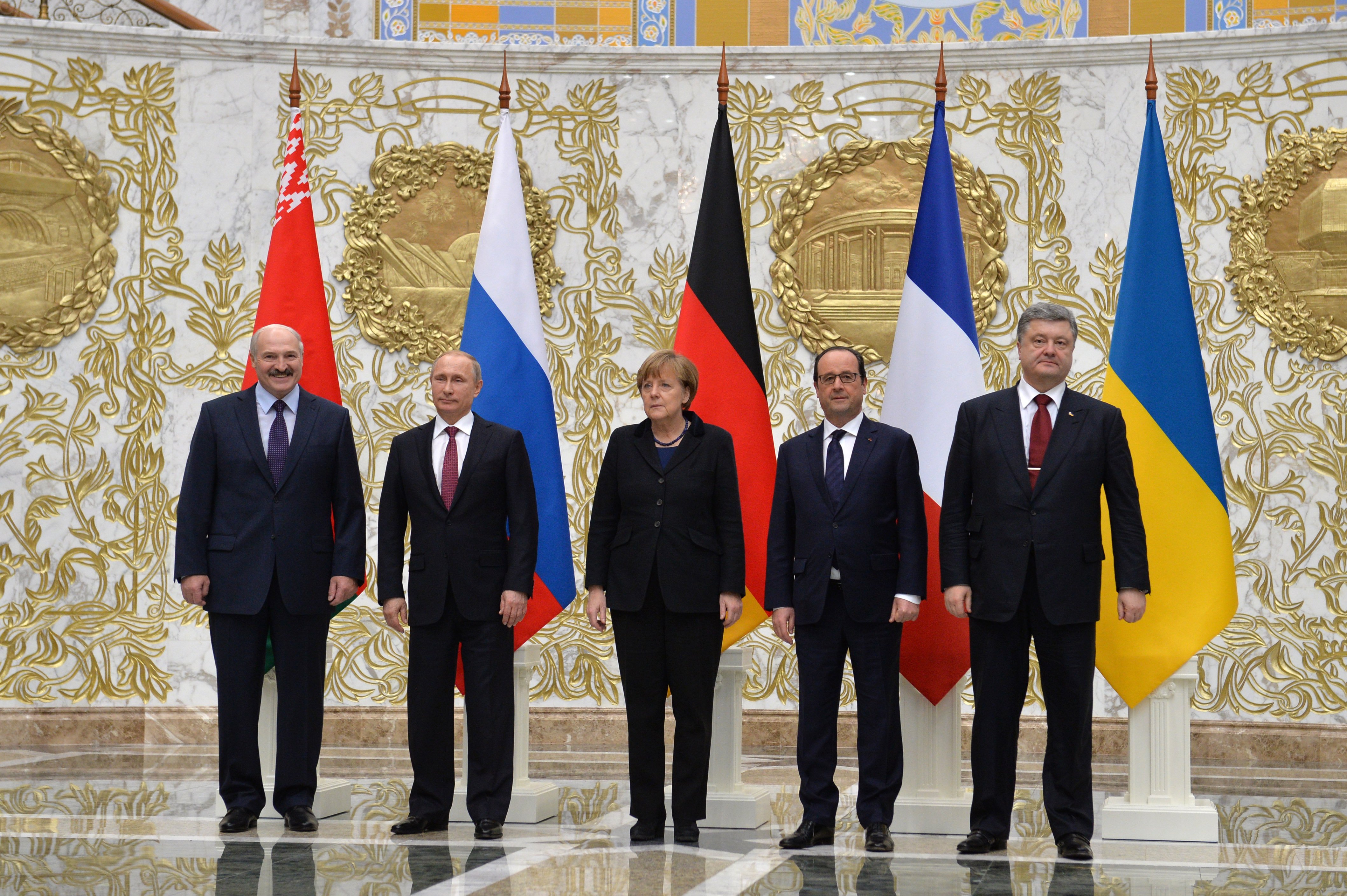 Aleksander Łukaszenko stoi obok innych liderów, w tym Putina, Merkel i Hollanda, z flagami Białorusi, Rosji, Niemiec, Francji i Ukrainy w tle.