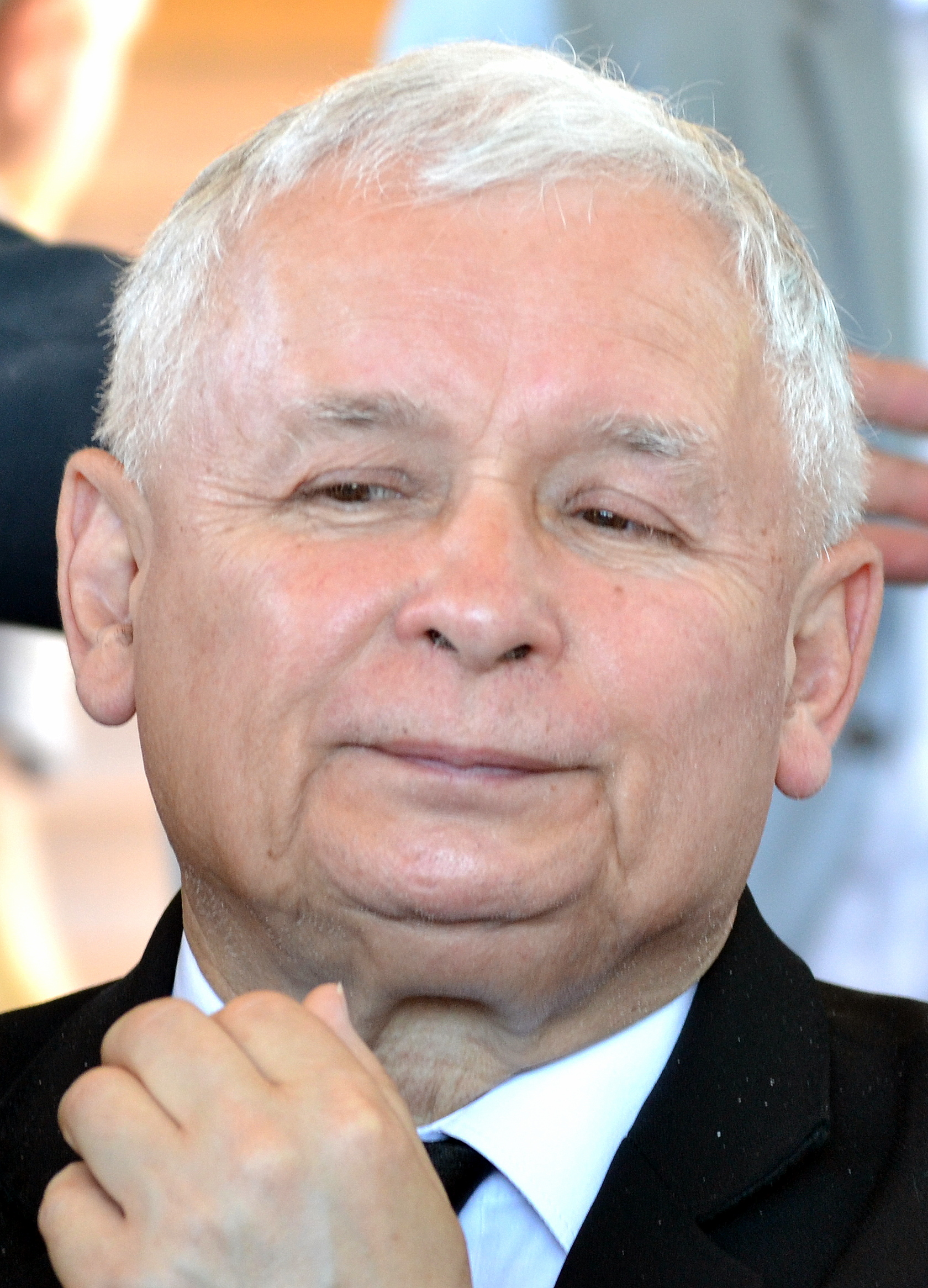 Jarosław Kaczyński w garniturze, z dłonią przy twarzy, podczas wypoczynku.