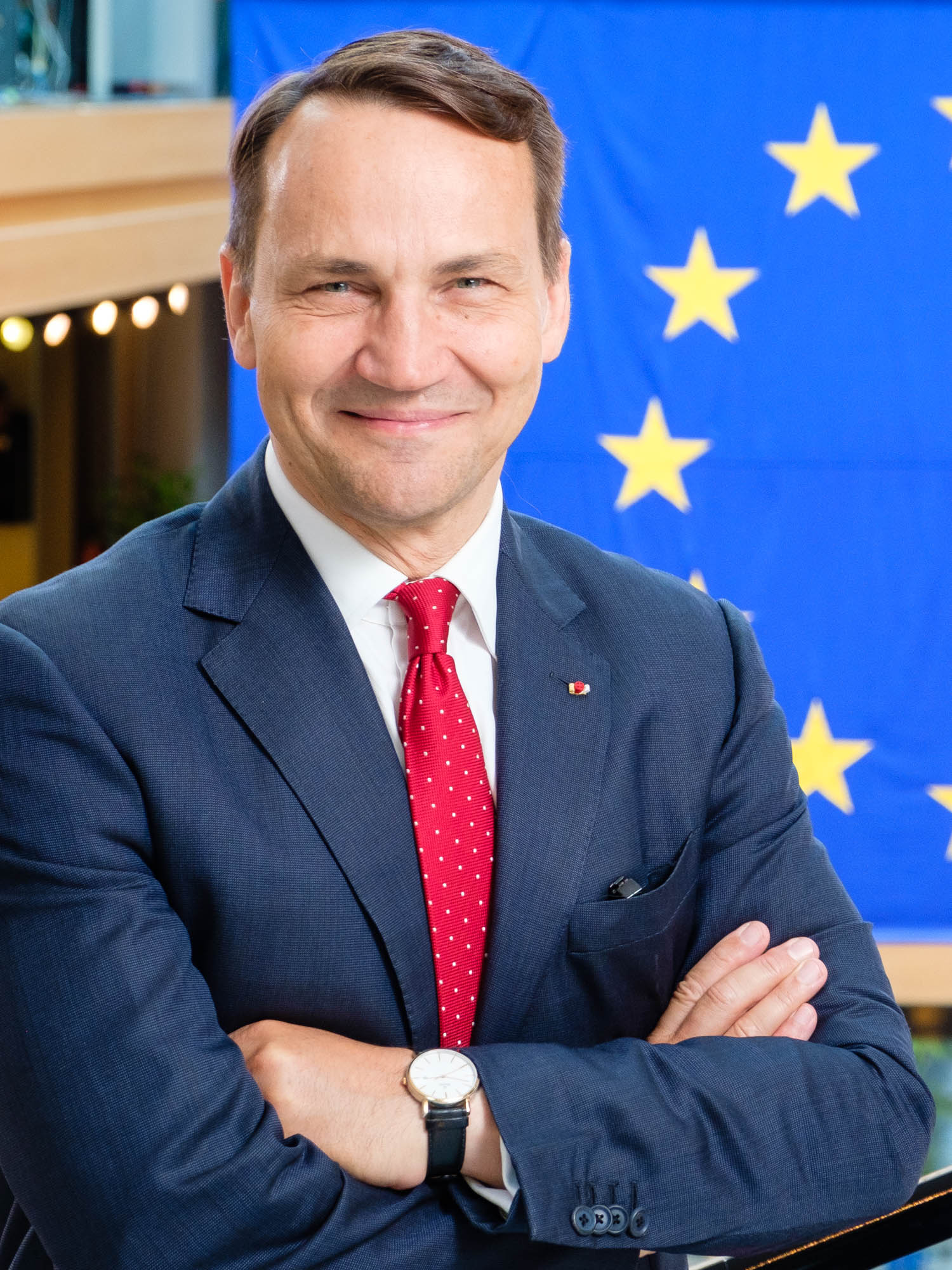 Radosław Sikorski z wizytą w USA: polski polityk na tle flagi UE.