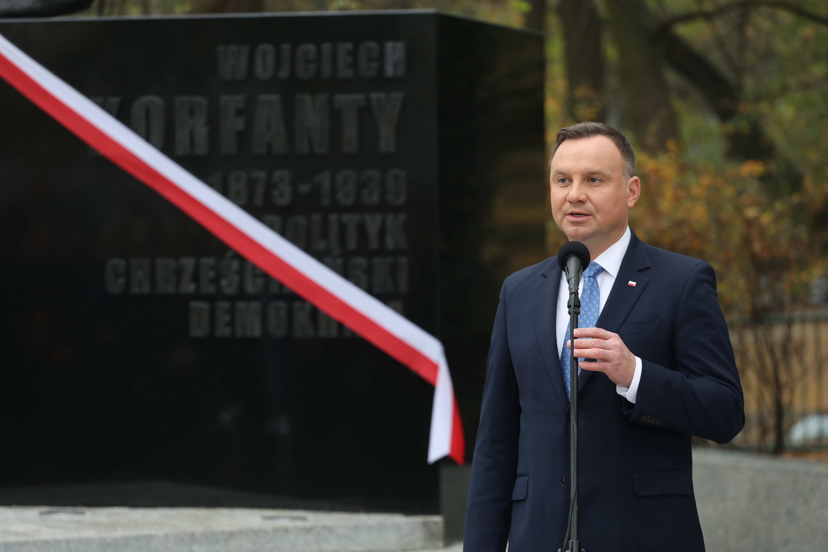 Prezydent Duda przemawia na tle pomnika z polską flagą – symbol weta prezydenta.