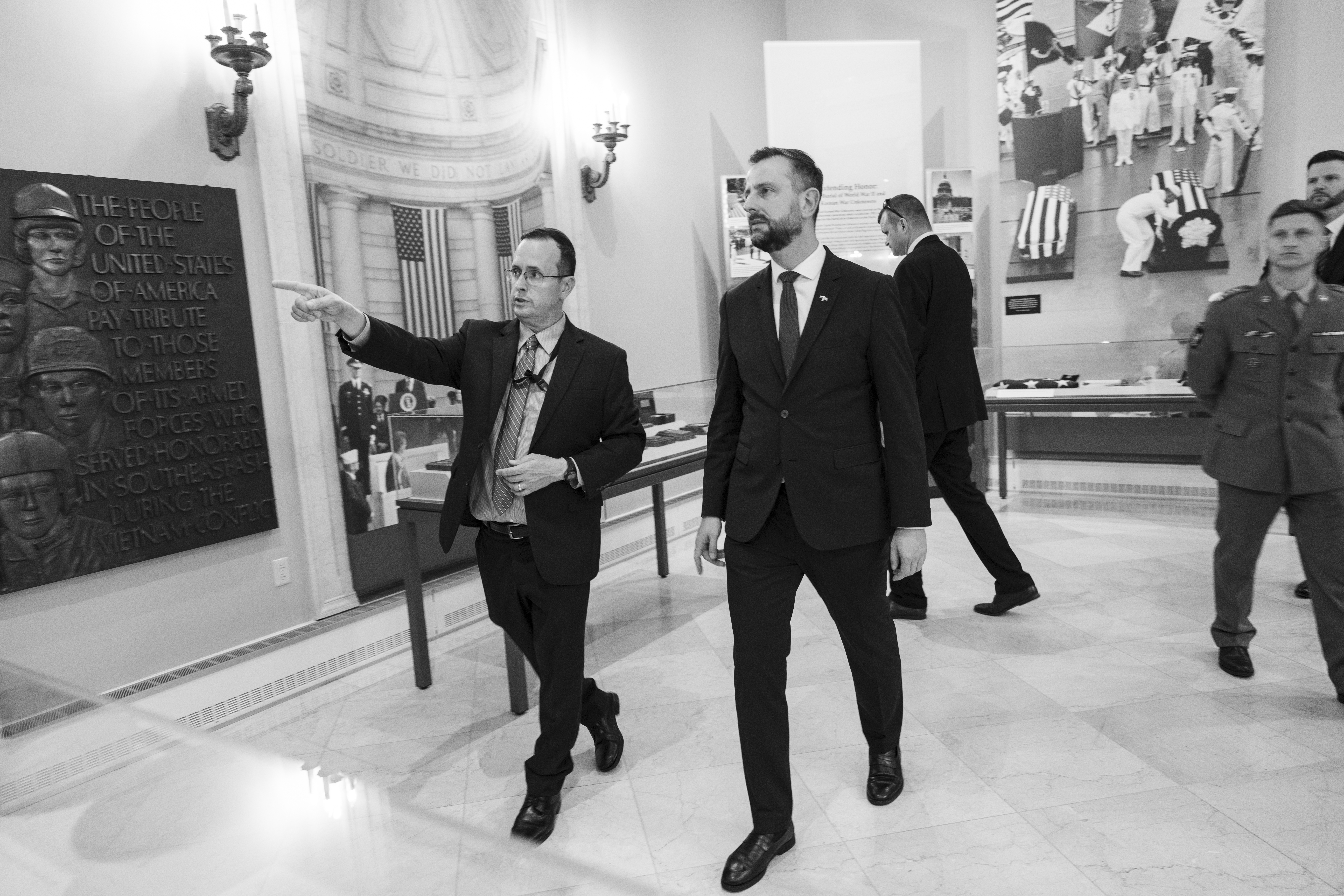 Szef MON i inni urzędnicy w garniturach podczas zwiedzania muzeum wojskowego.