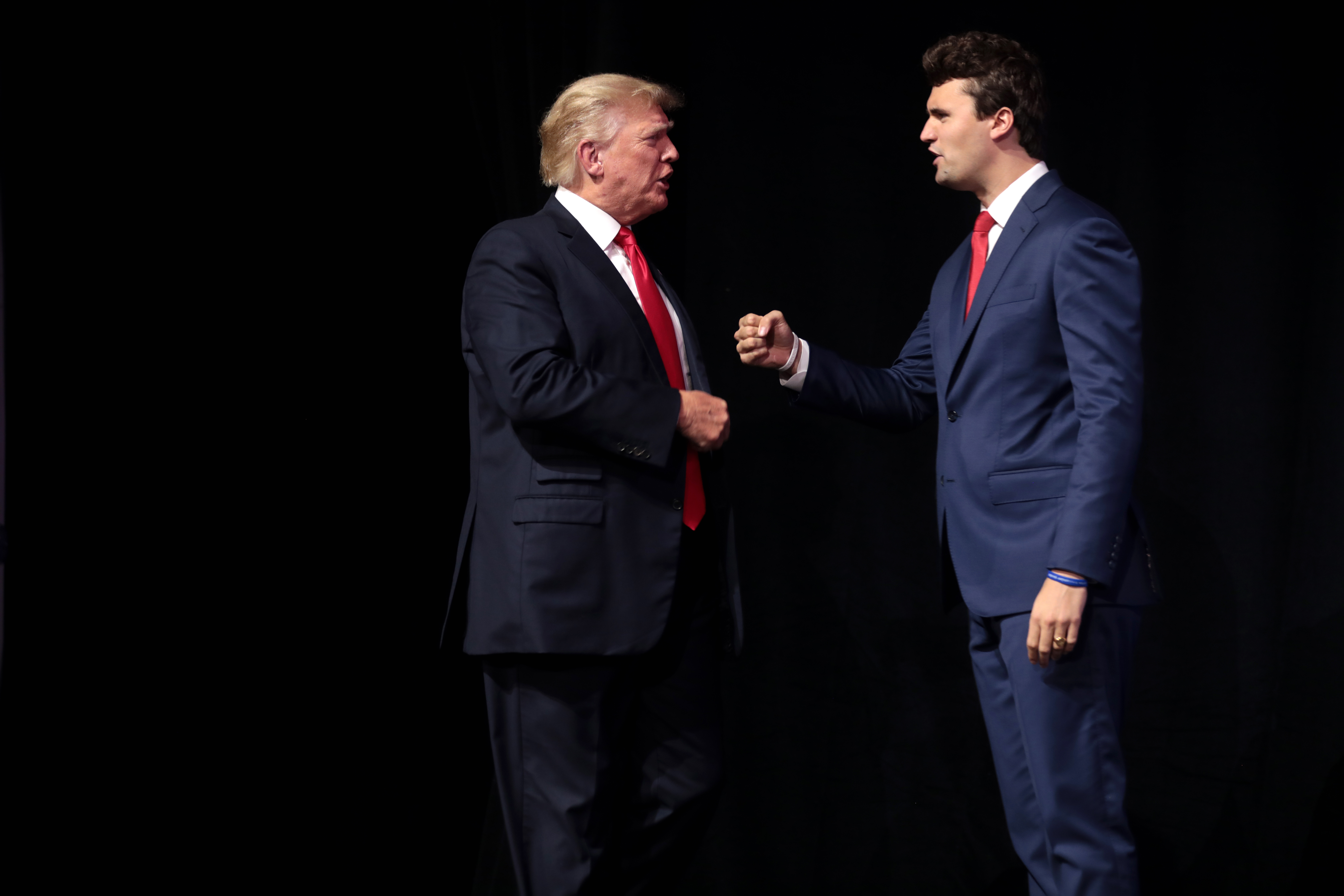 Donald Trump i Charlie Kirk rozmawiający na czarnym tle.