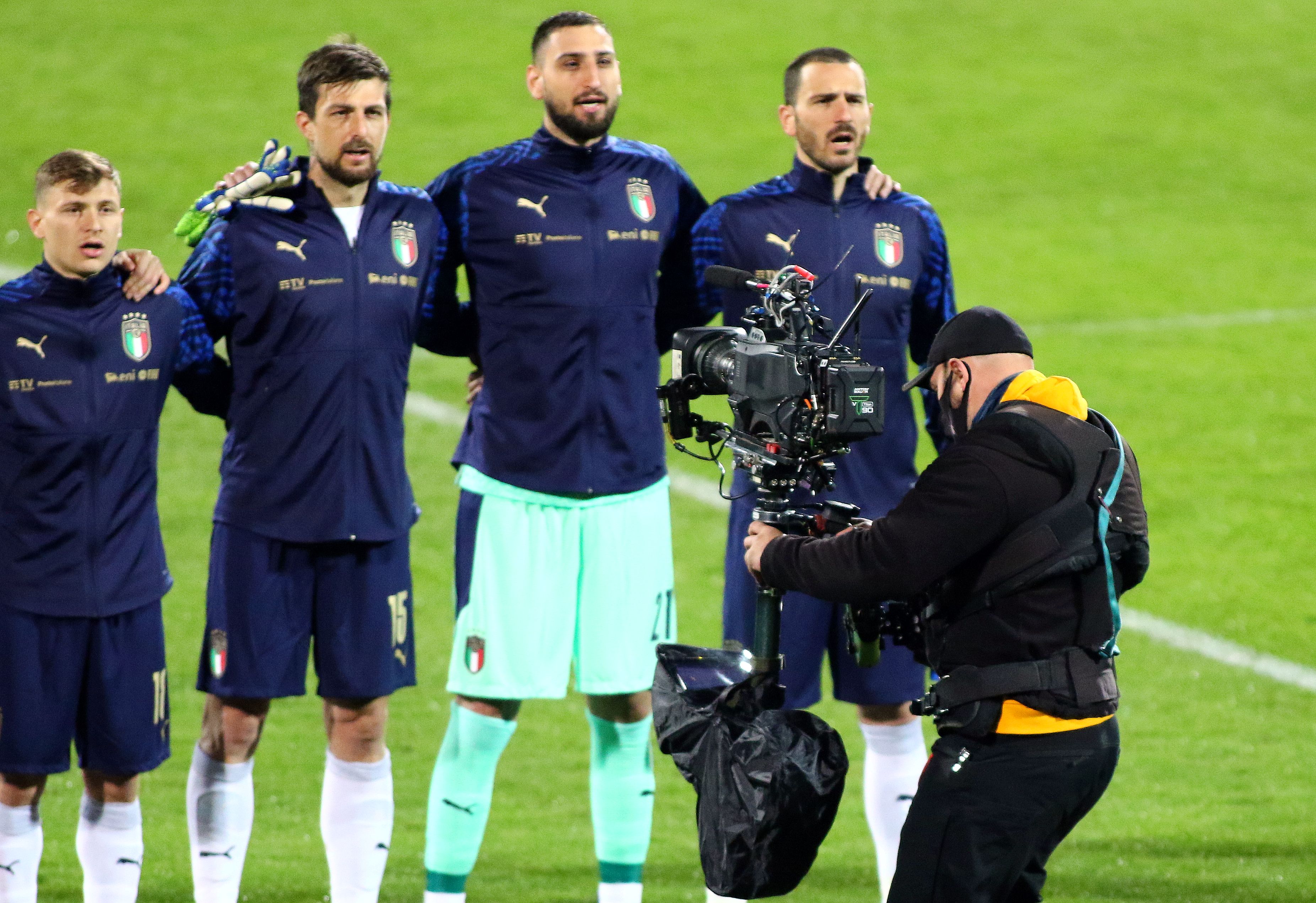 Gianluigi Donnarumma z drużyną Włoch na boisku, przygotowuje się do meczu, z kamerą filmową w tle.