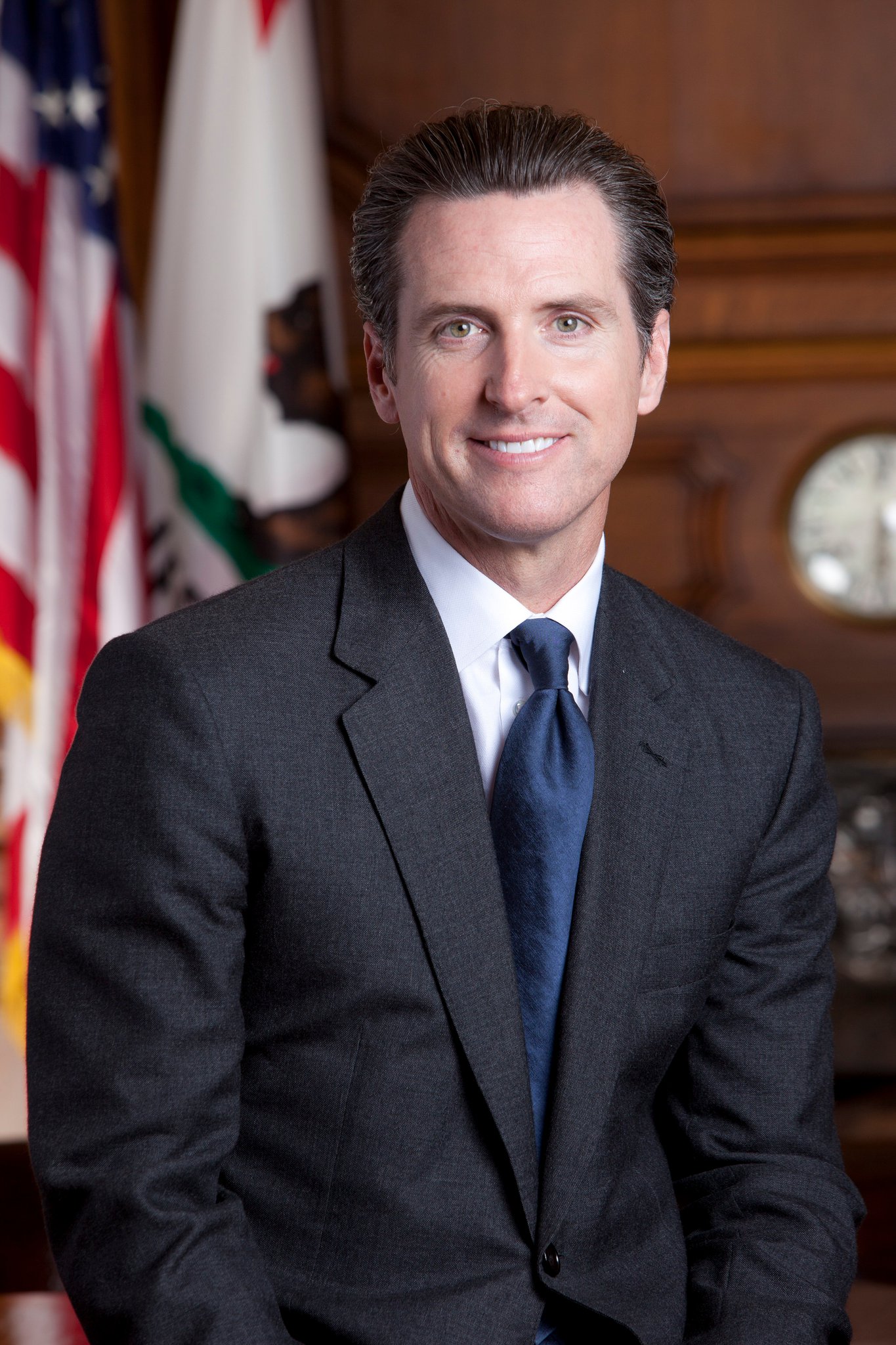 Gubernator Gavin Newsom w garniturze, na tle flagi USA i Kalifornii, alarmuje o przyszłości demokracji.