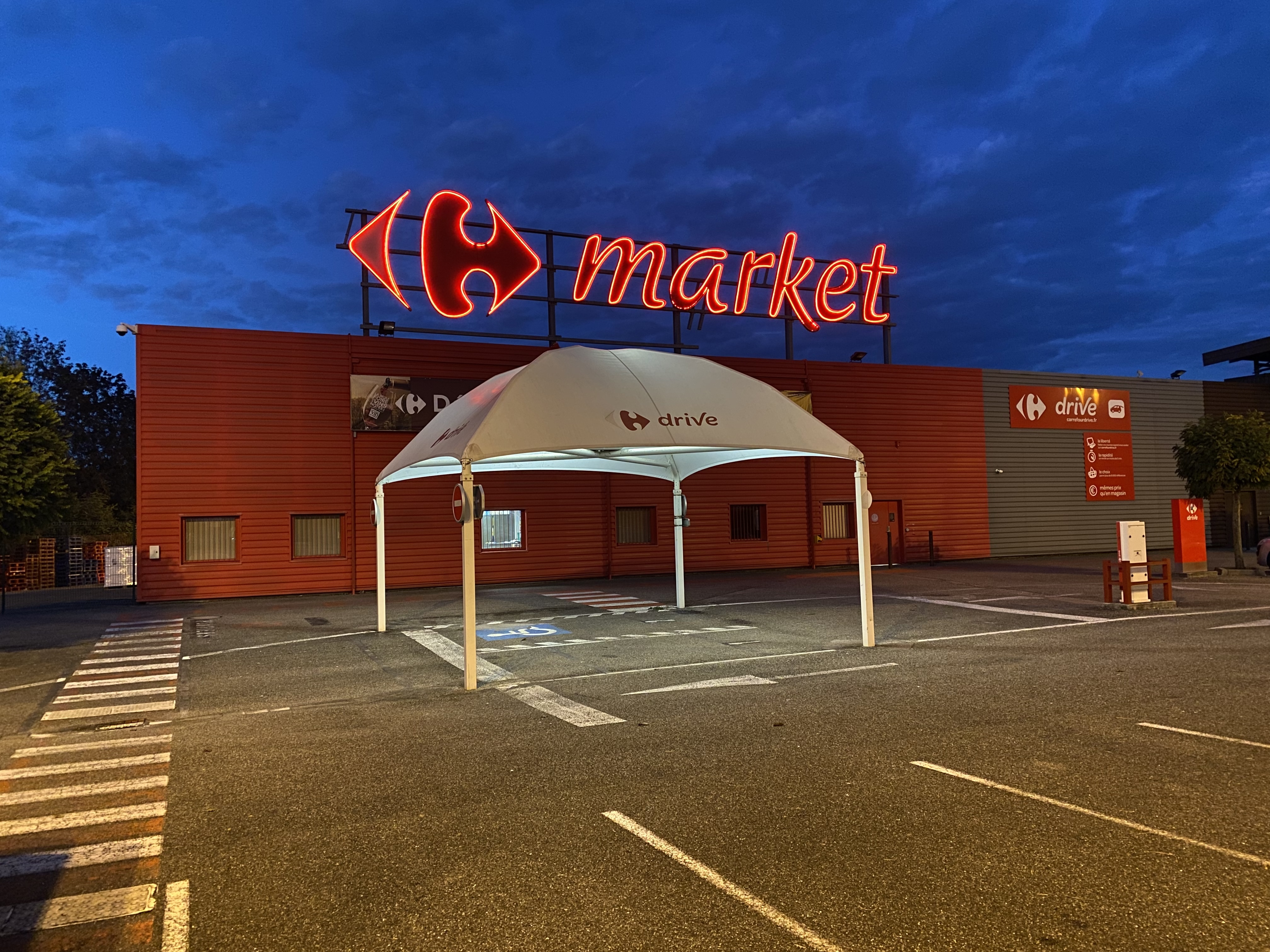 Neonowy znak Carrefour Market i zadaszenie Drive-thru przed sklepem