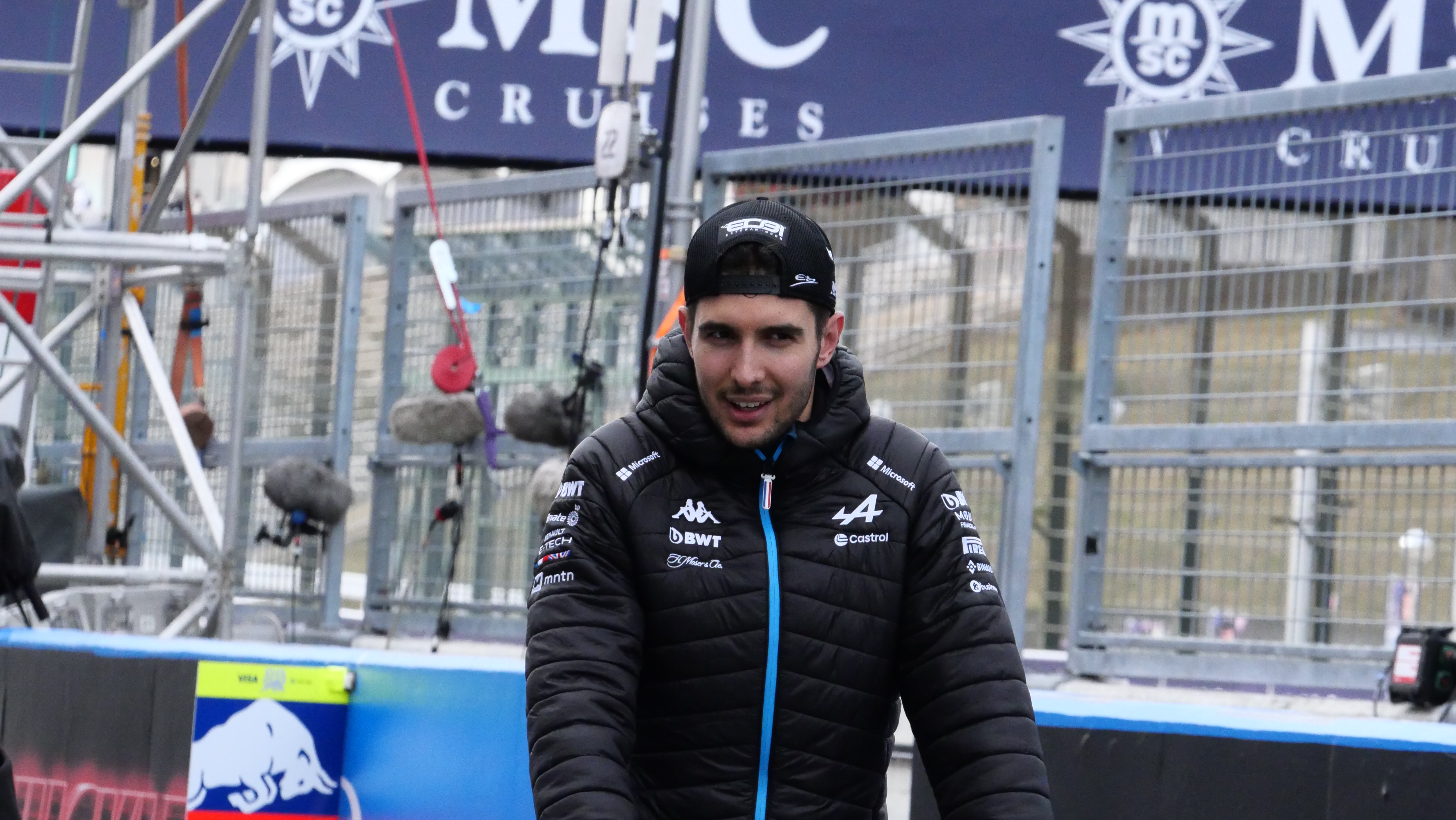 Esteban Ocon w kurtce zespołu Alpine na tle padoku F1, po skandalu z bolidem.