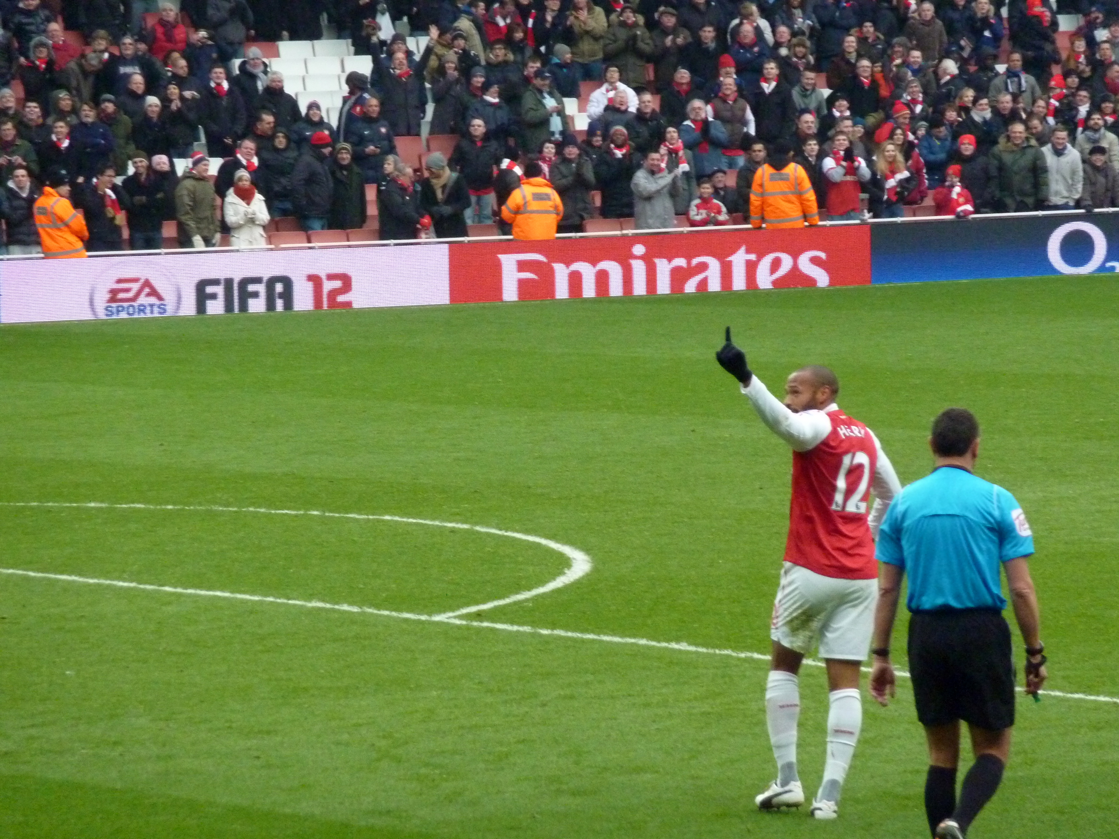 Thierry Henry na boisku piłkarskim, wskazujący palcem w górę.