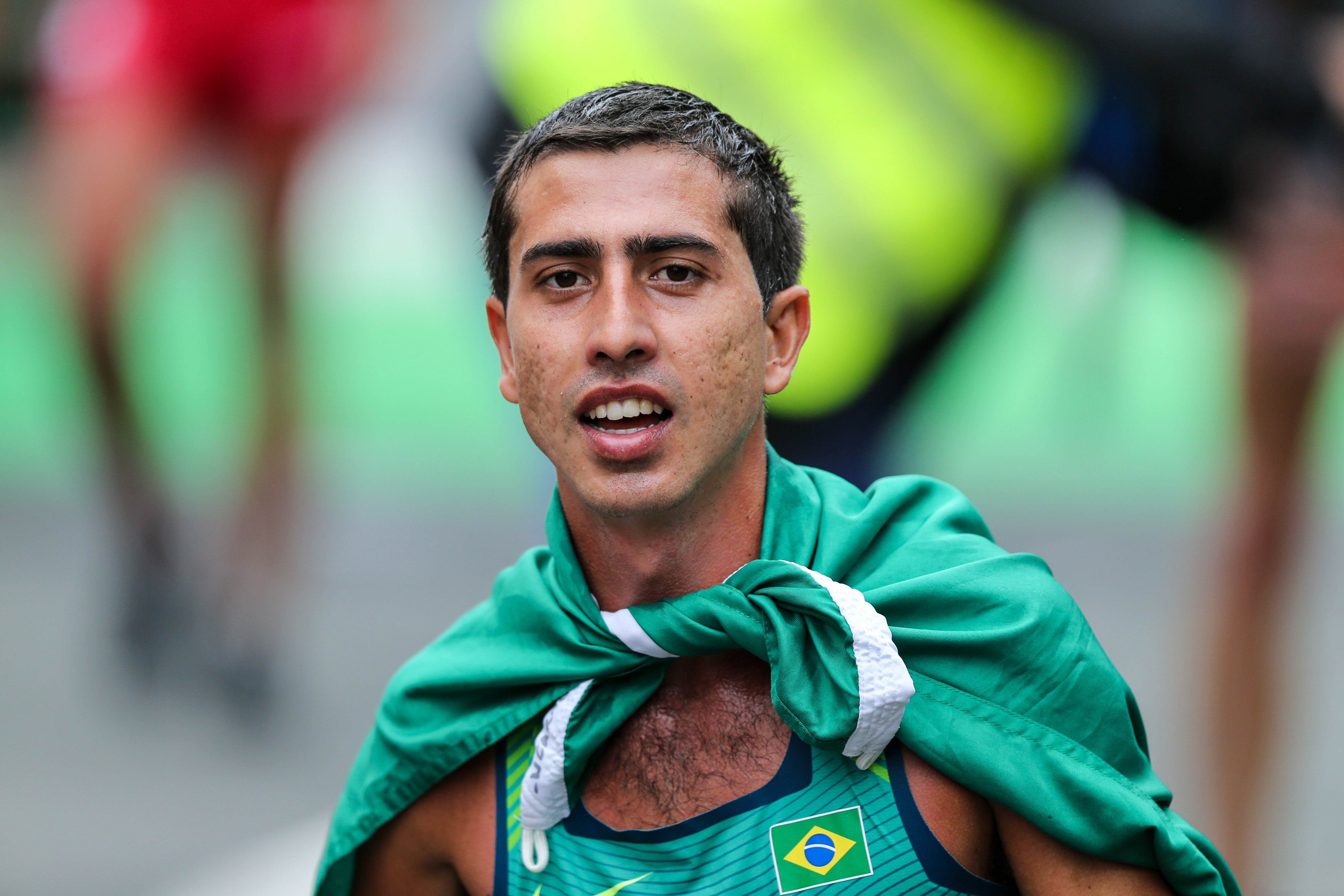 Brazylijczyk Caio Bonfim w zielonej pelerynie z flagą Brazylii, świętuje złoty medal w chodzie sportowym.
