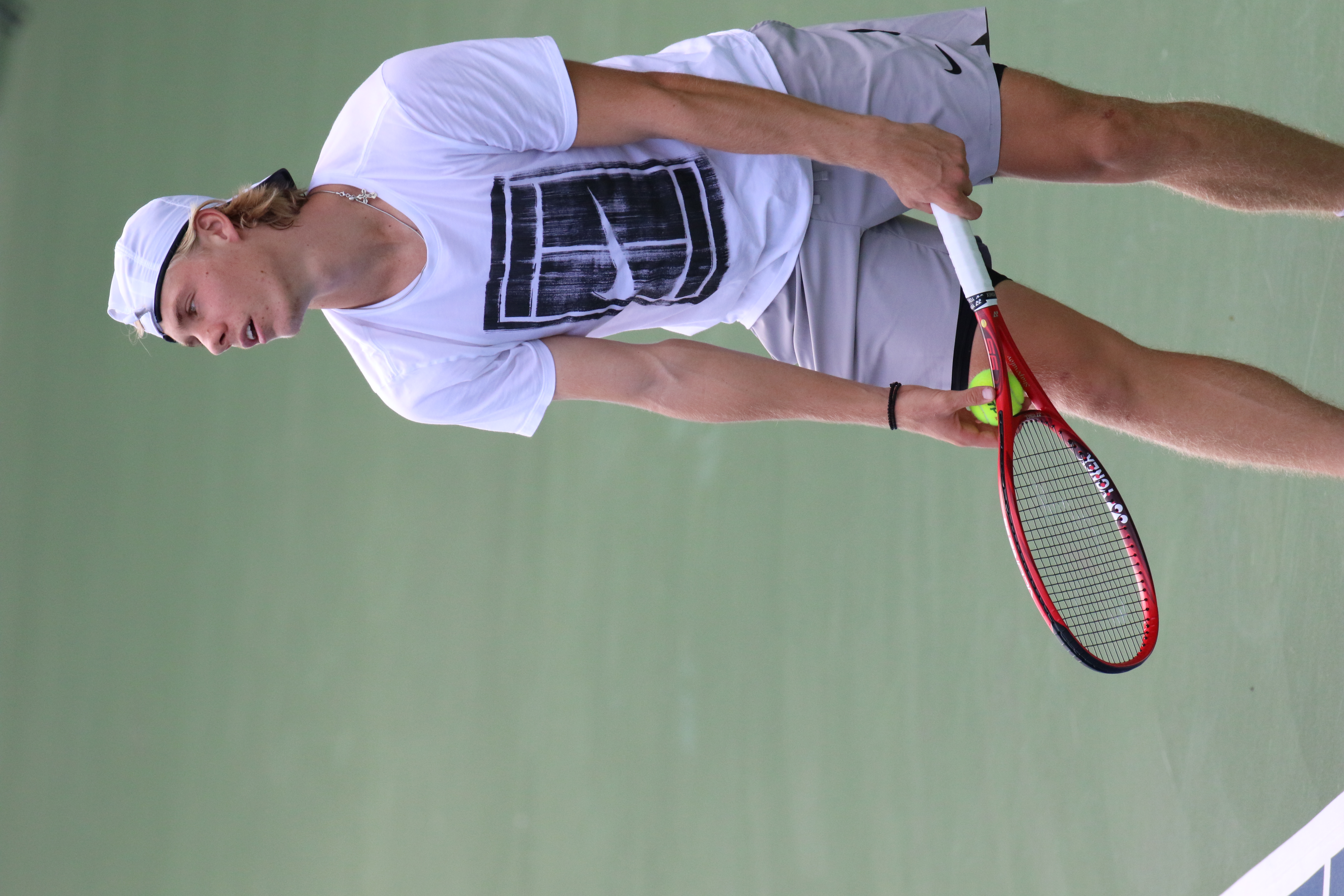Denis Shapovalov, tenisista, podczas serwisu z rakietą i piłką tenisową na korcie.