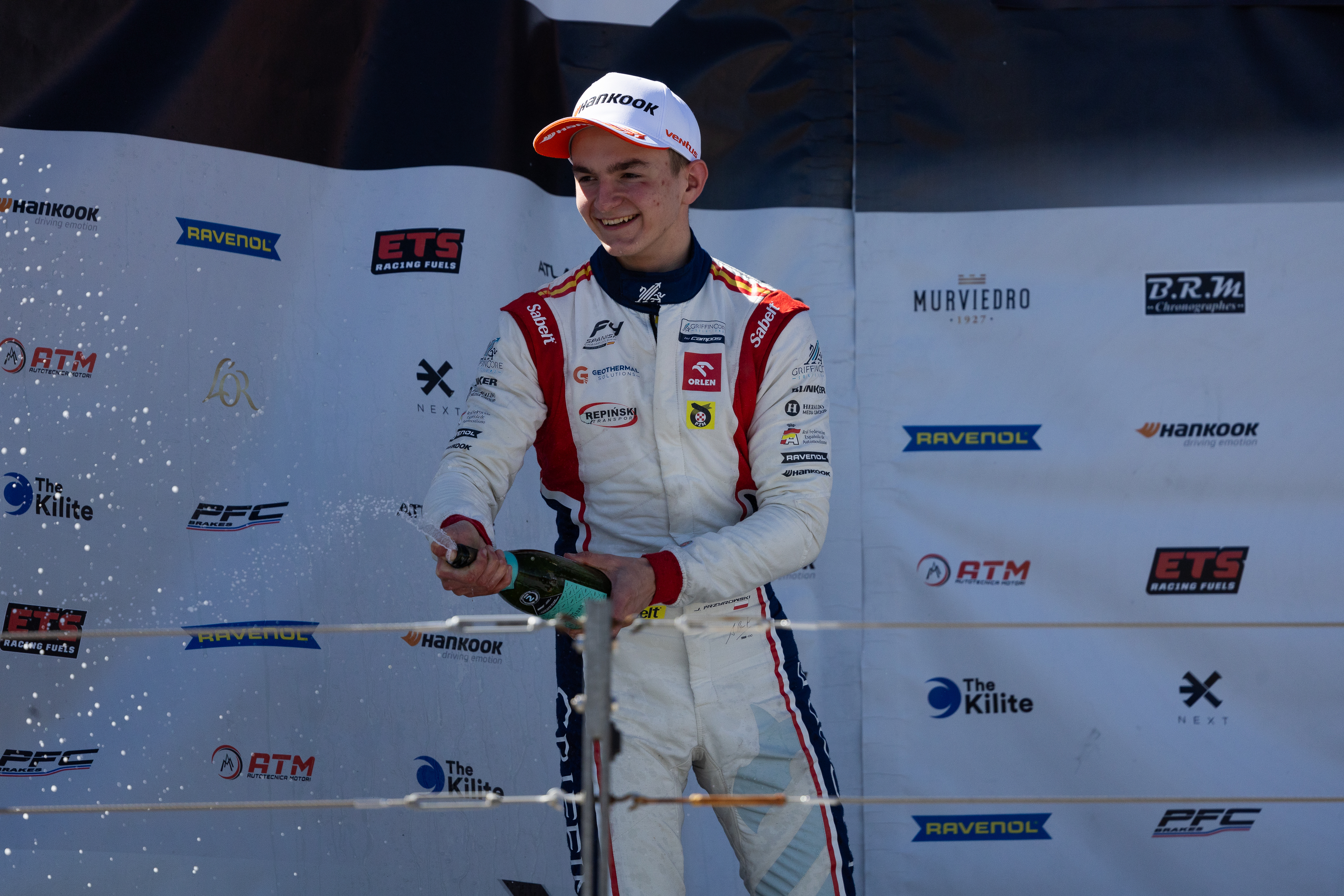 Jan Przyrowski świętuje na podium, rozlewając szampana po zdobyciu pole position.