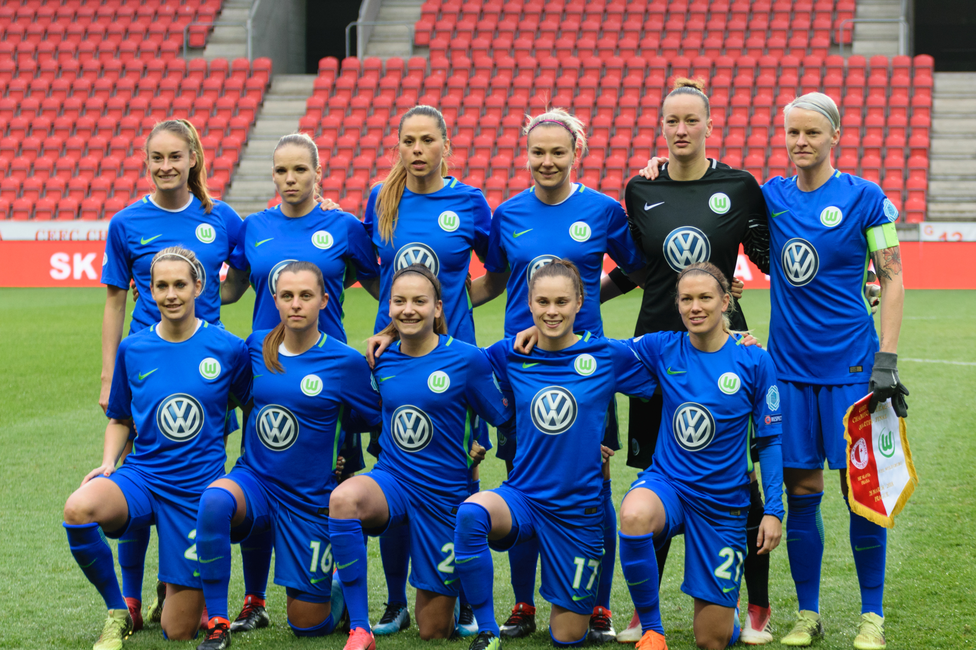 Drużyna piłkarska VfL Wolfsburg kobiet w niebieskich strojach pozuje do zdjęcia na boisku, z Ewa Pajor w centrum.