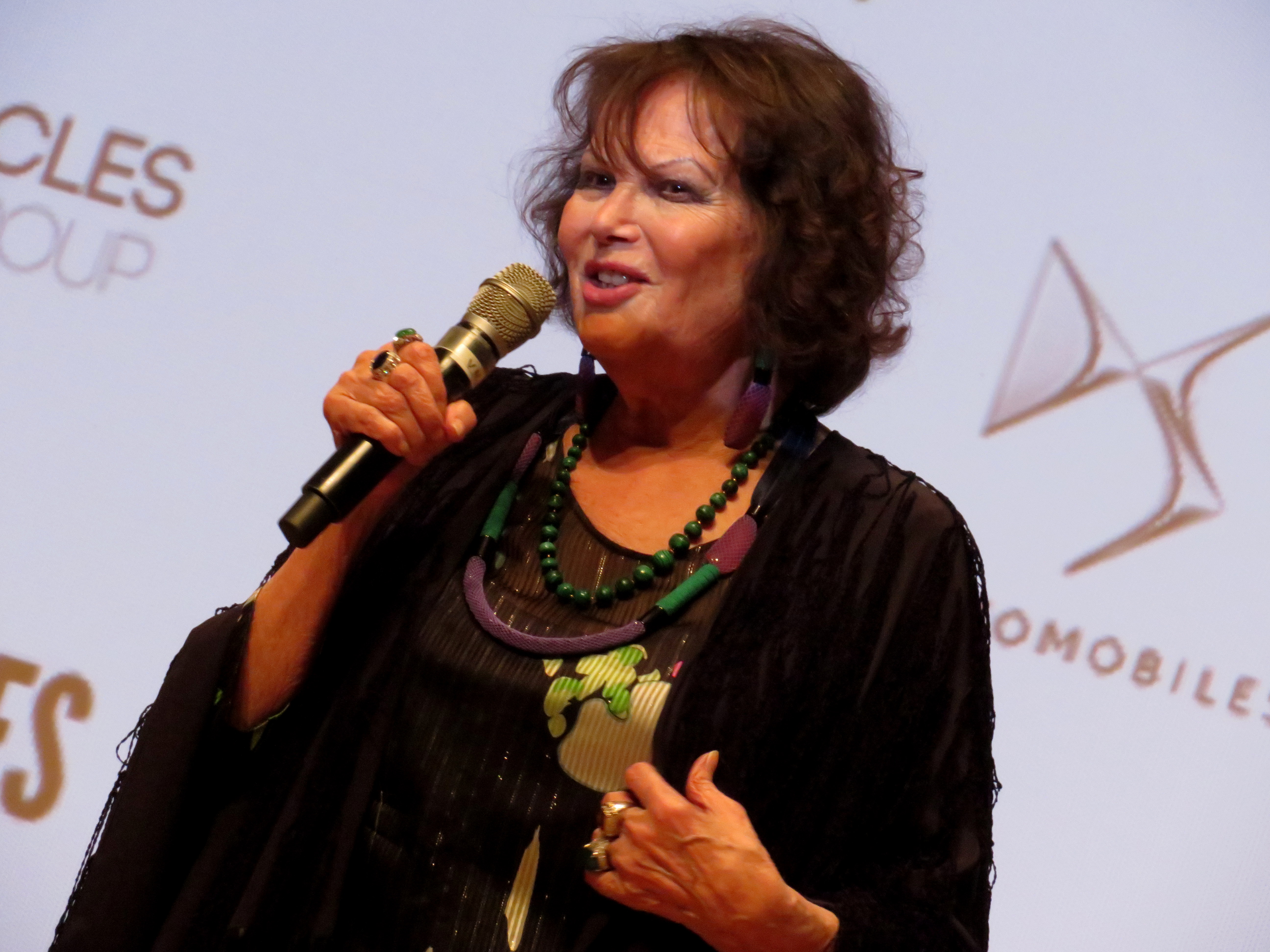 Claudia Cardinale, ikona kina, przemawia do mikrofonu, dementując plotki o śmierci.