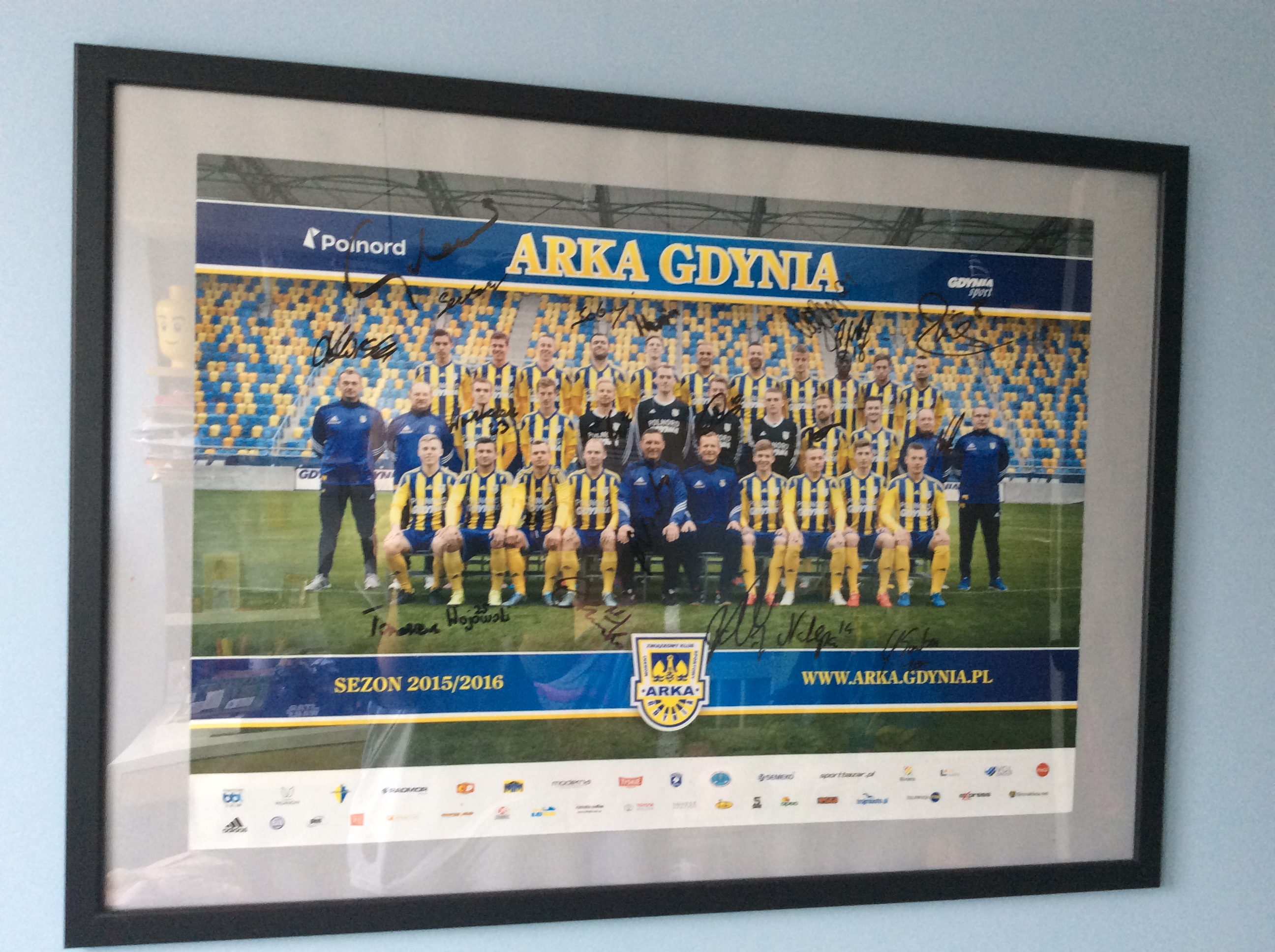 Drużyna Arki Gdynia z sezonu 2015/2016, z autografami zawodników, na tle trybun.