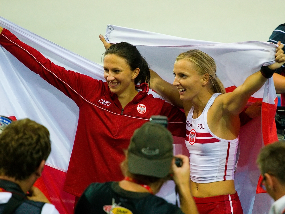 Monika Pyrek i inna sportsmenka trzymają polską flagę, celebrując sukces sportowy.