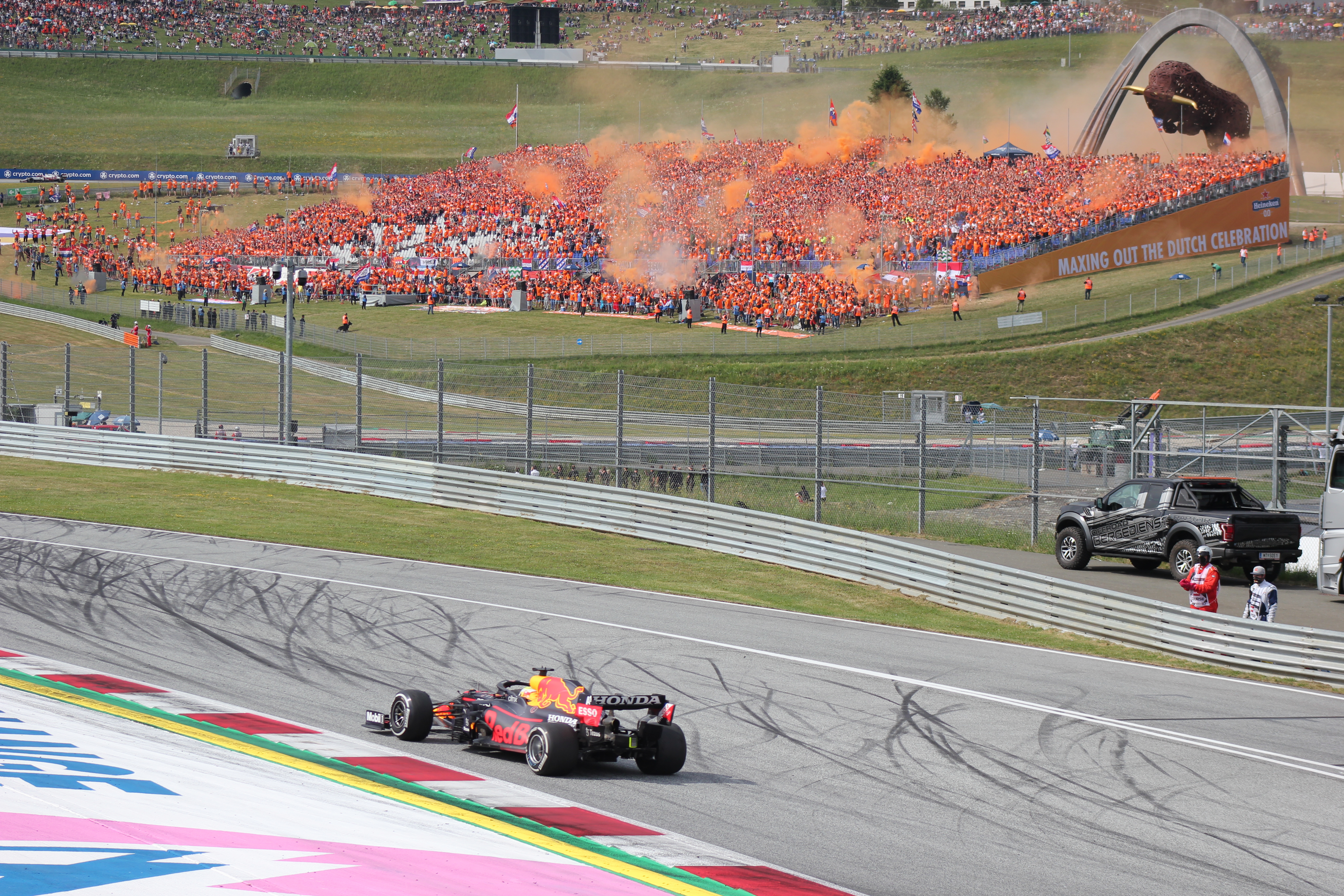 Max Verstappen w bolidzie Red Bull Racing na torze podczas wyścigu F1, z kibicami świętującymi w tle.