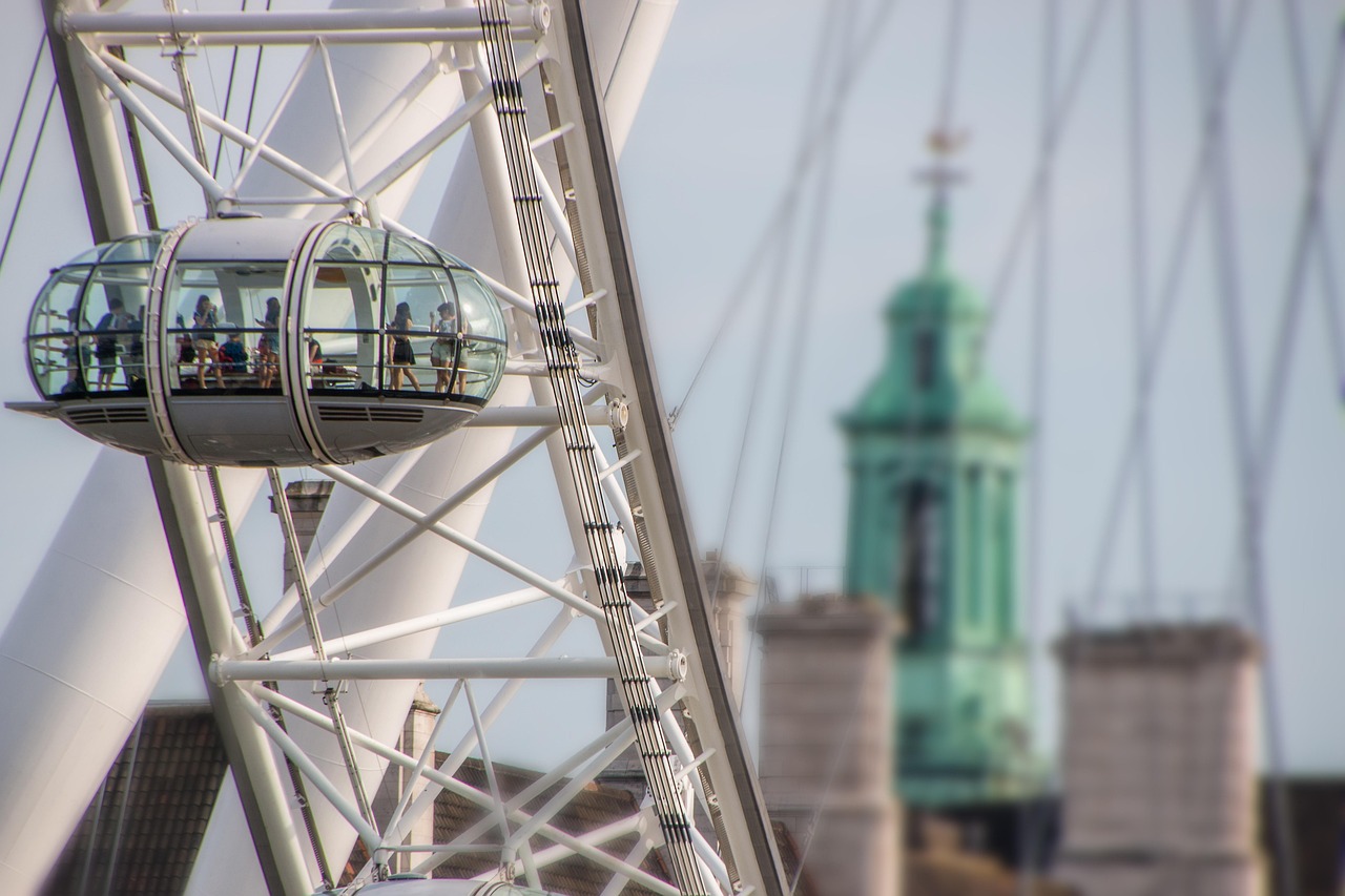 Widok na London Eye z kapsułą i zieloną wieżą w tle, symbolizującą Londyn.